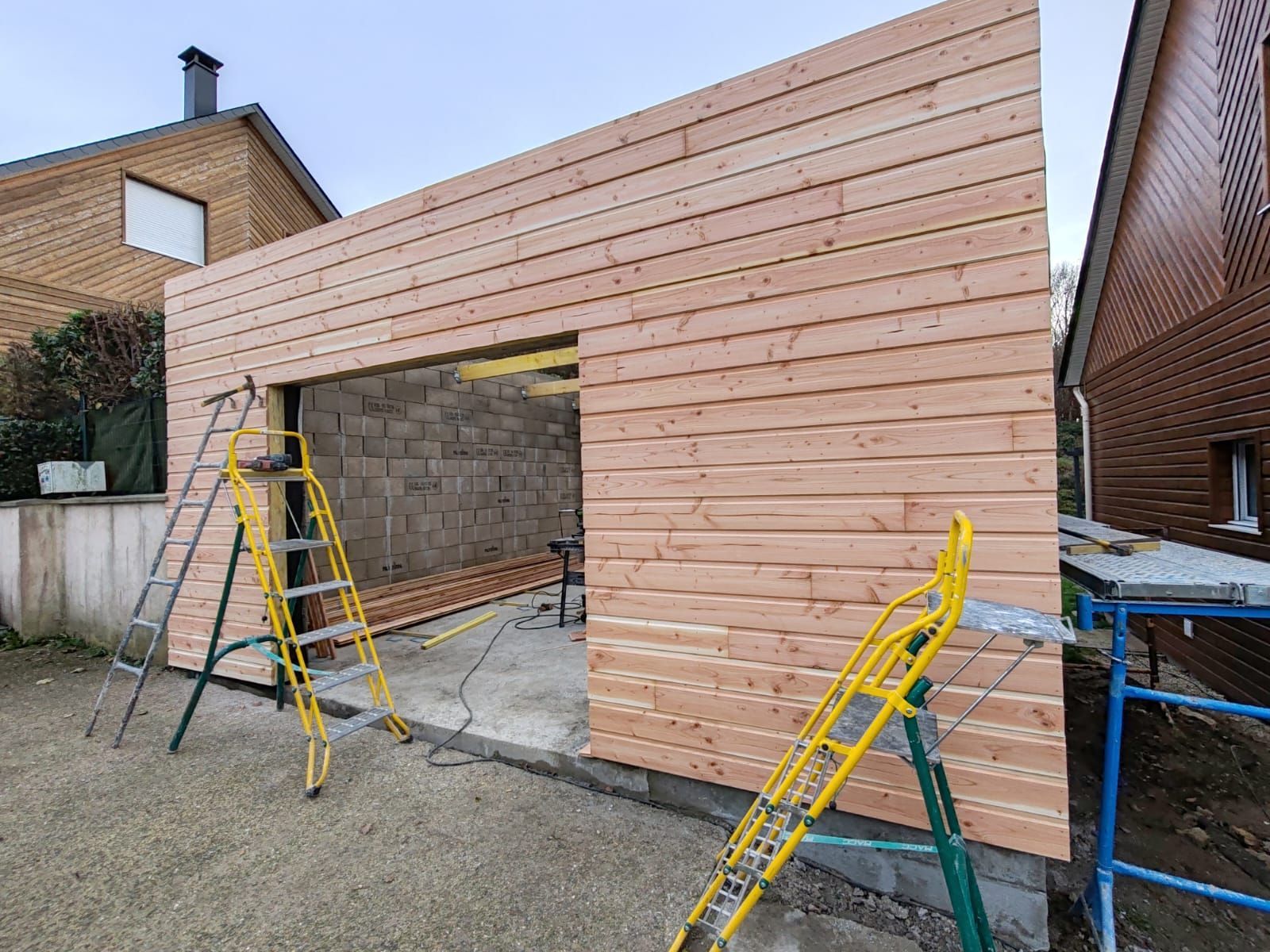 Façade de garage en bois en construction avec échelles, échafaudages et porte partiellement ouverte