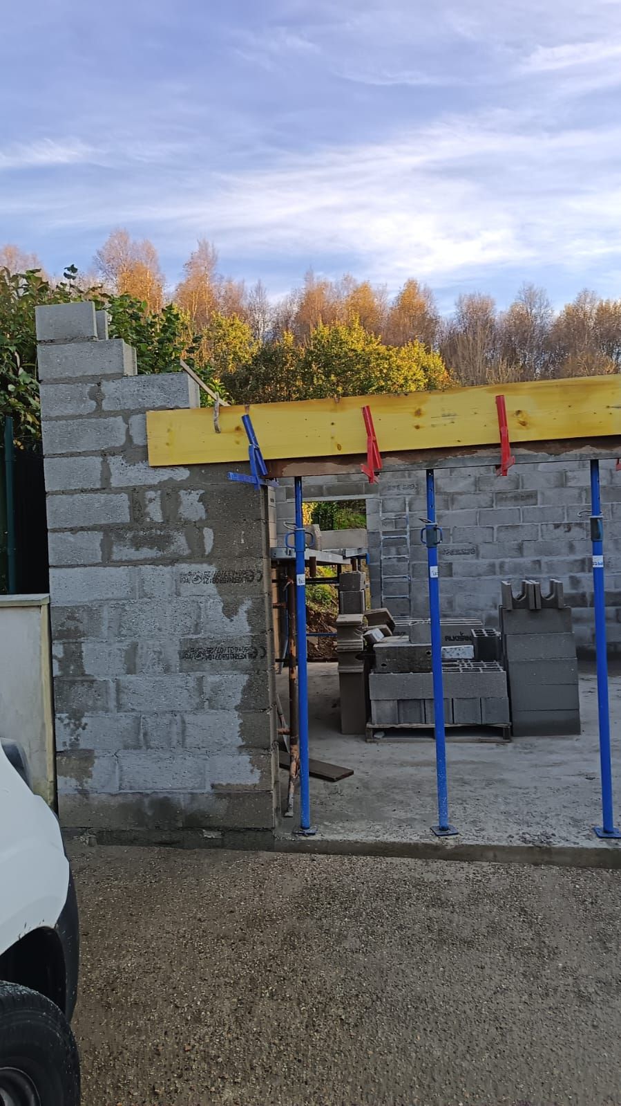 Mur en parpaings partiellement construit, avec poutres jaunes et supports bleus, sur un chantier de construction.
