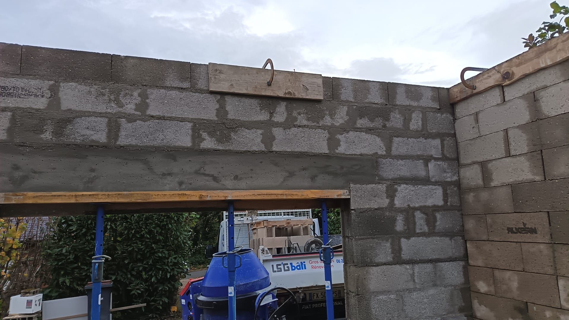Porte en parpaings partiellement construite, recouverte d'une bâche bleue, avec des matériaux de construction visibles à travers l'ouverture.