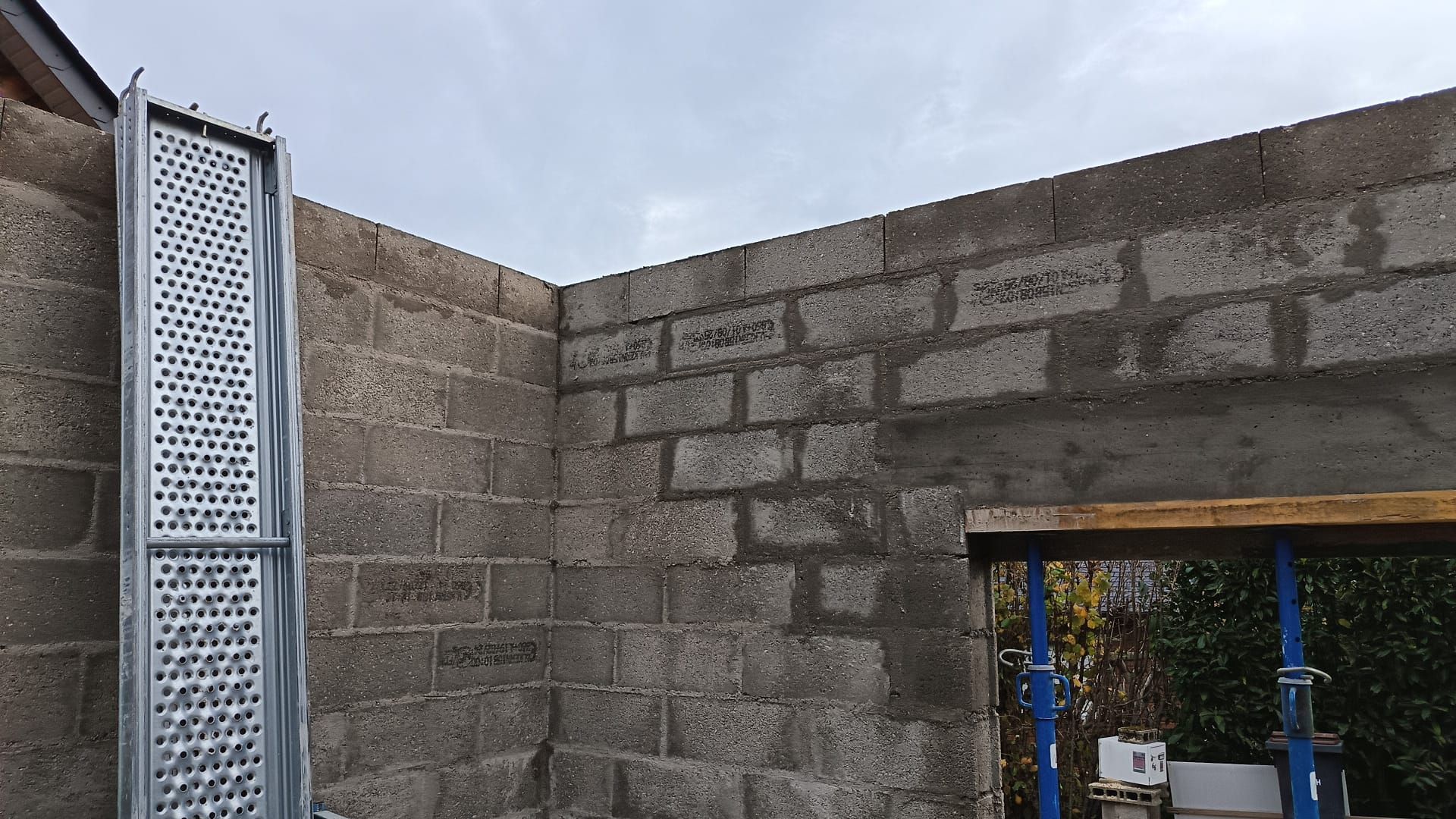 Mur en parpaings partiellement construit, avec un portail métallique et une fenêtre donnant sur une cour.