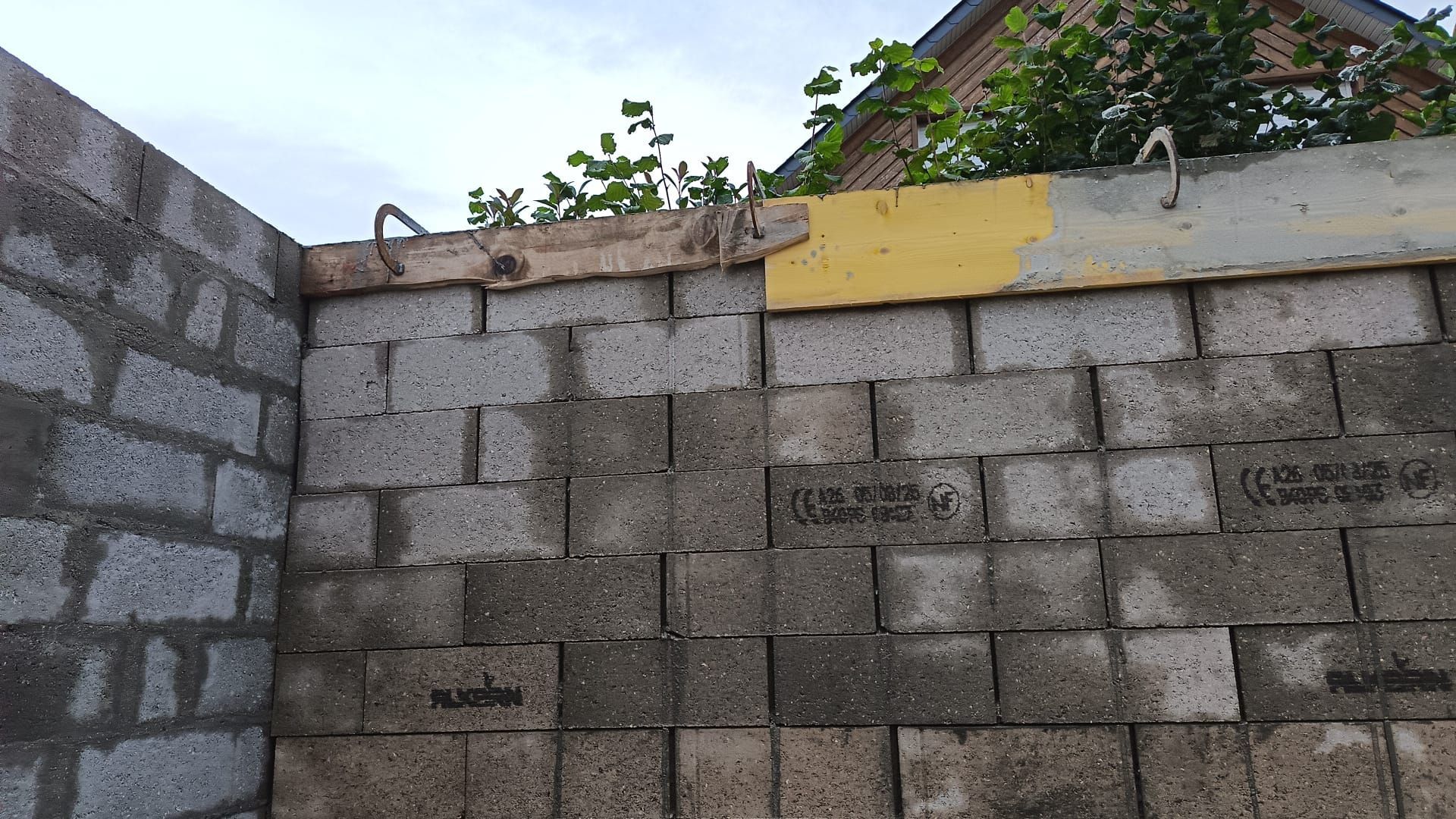 Mur en parpaings gris avec une partie supérieure jaune et des arbres visibles au-dessus.