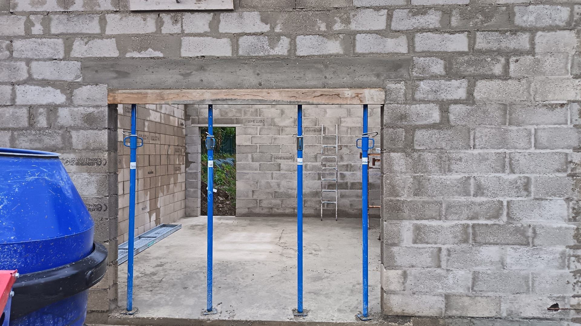Mur en pierre avec une porte étroite bloquée par des barreaux métalliques bleus, avec une poubelle bleue sur la gauche.