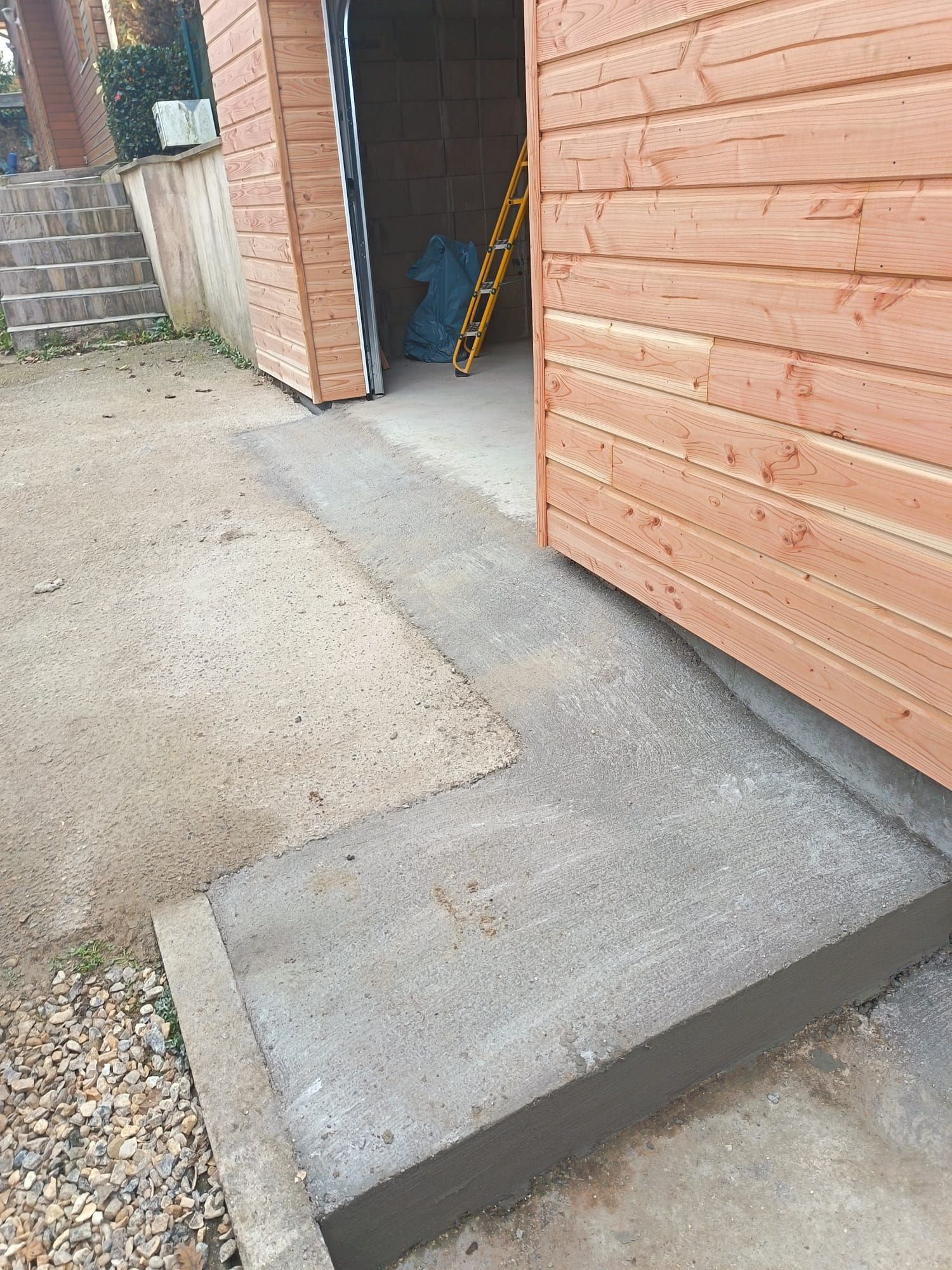 Marche en béton menant à un garage en bois, avec porte ouverte et allée pavée.
