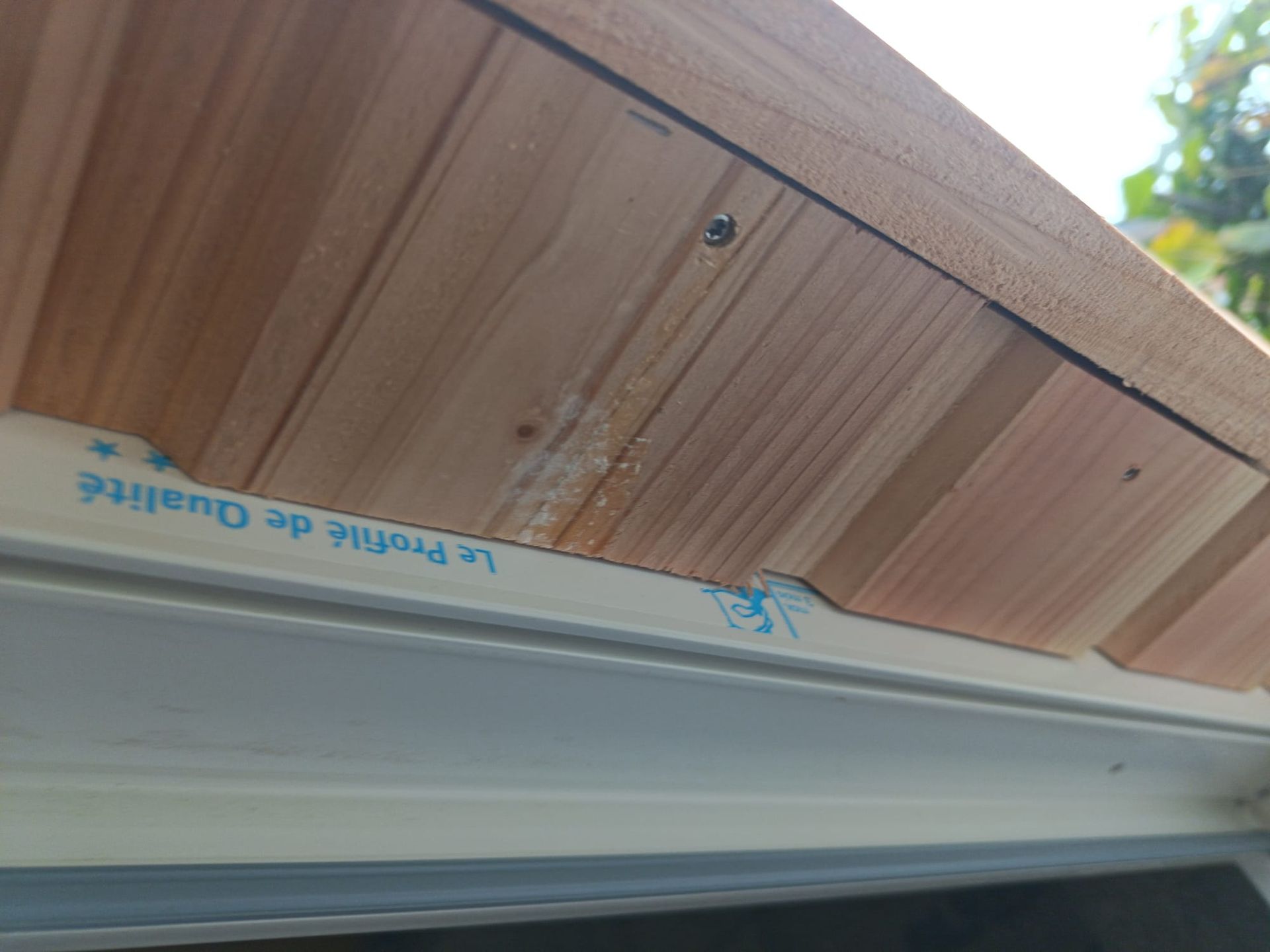 Gros plan sur un soffite en bois sous un avant-toit, avec un ruban adhésif de protection bleu sur la moulure.