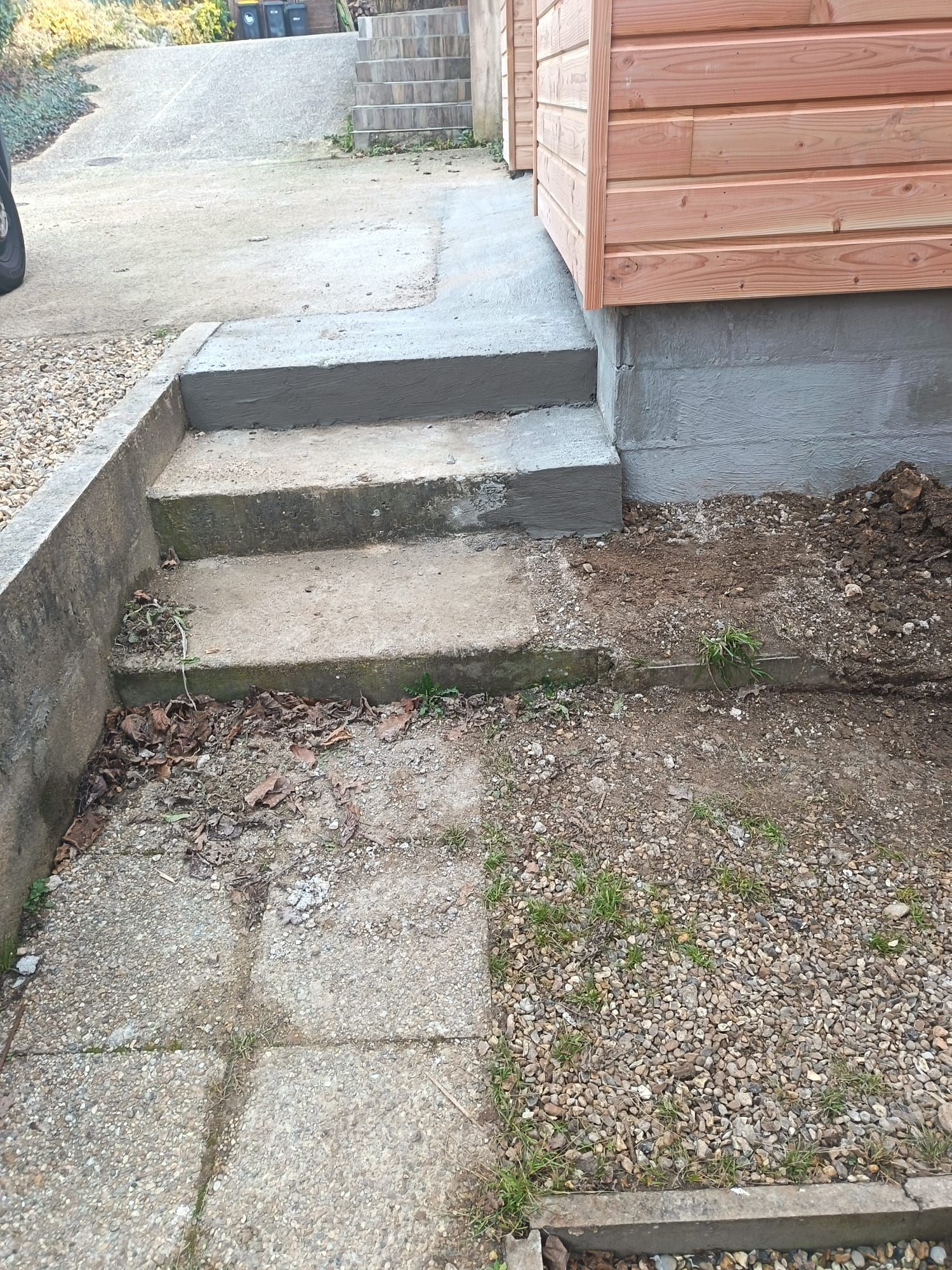 De petites marches en béton longent un chemin de gravier et un mur d'enceinte en bois à l'extérieur.