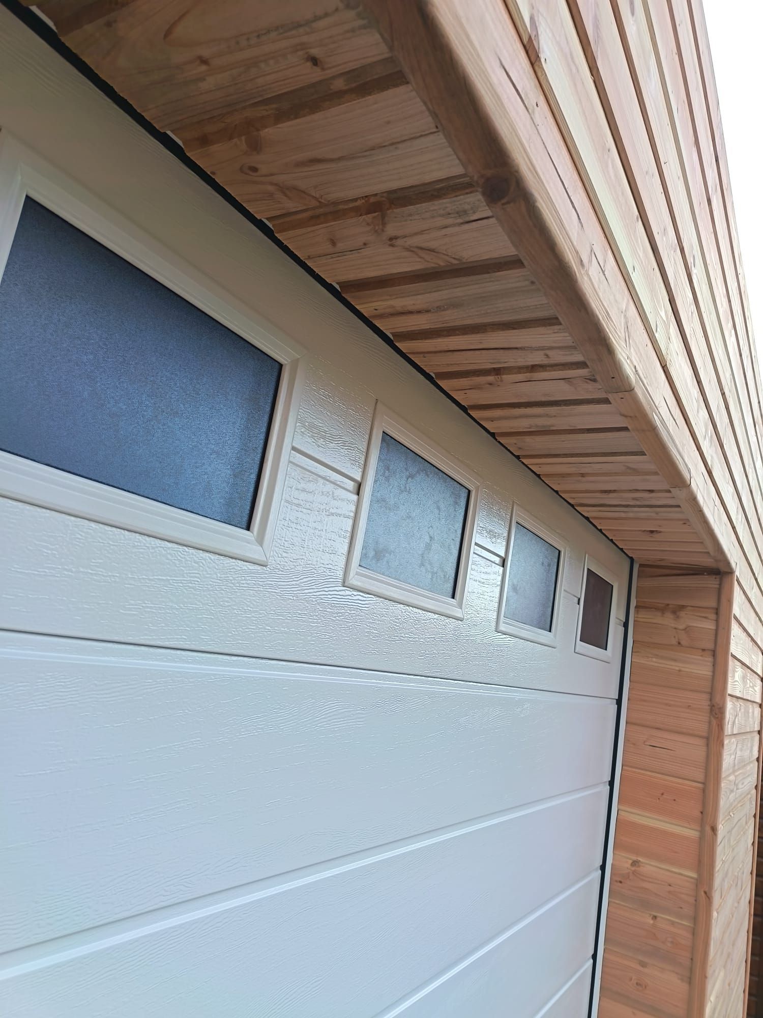 Porte de garage blanche avec vitres dépolies sous un auvent en bois sur une maison moderne