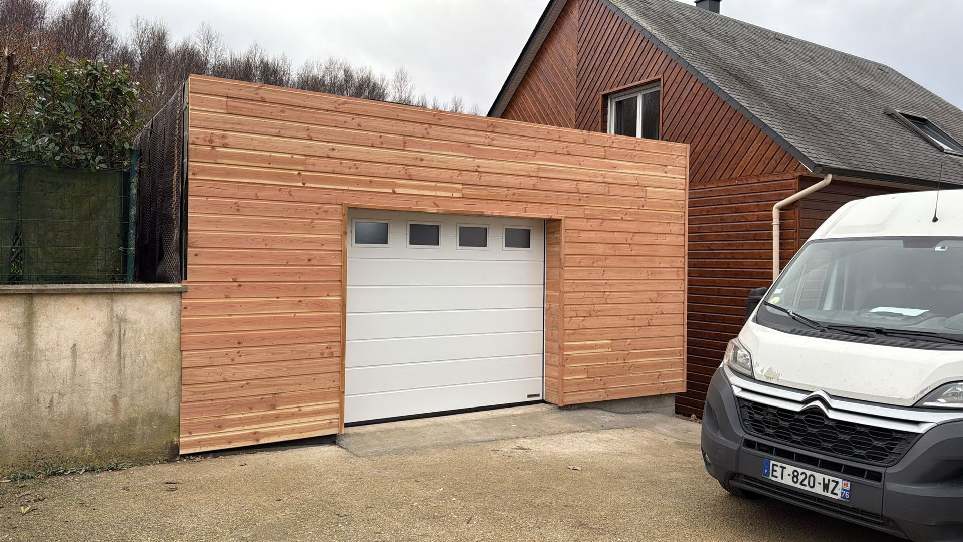 Façade de garage en bois avec une porte blanche à côté d'une camionnette blanche garée dans une allée.