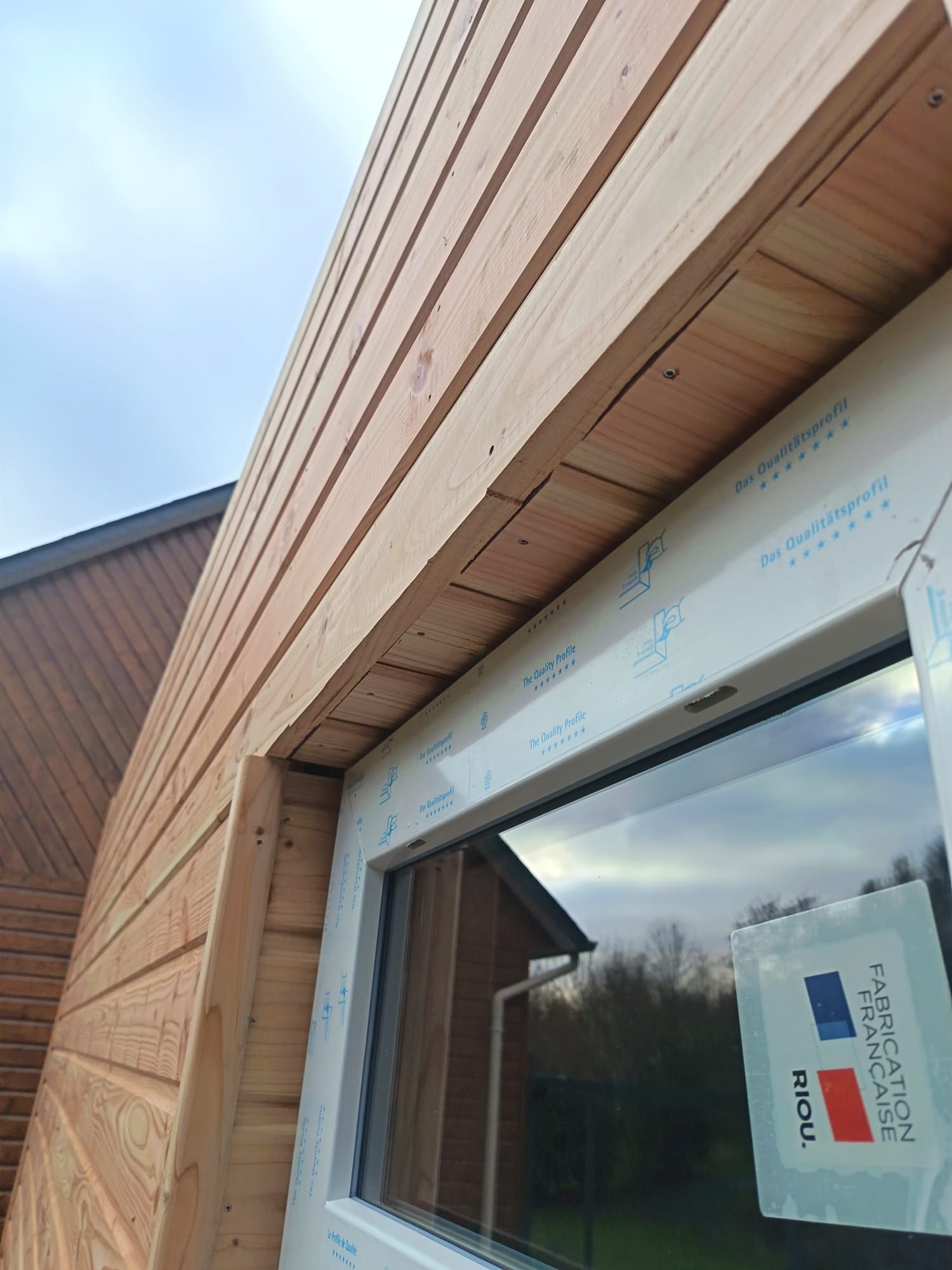 Coin d'un bâtiment revêtu de bois avec un cadre de fenêtre en construction sur fond de ciel nuageux