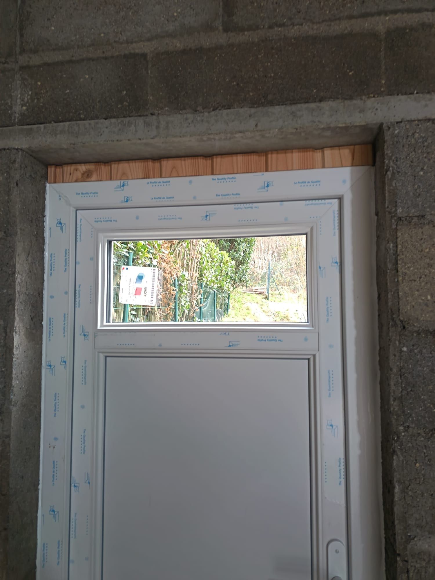 Porte blanche avec une petite fenêtre, encadrée de mousse de construction sous un linteau en béton.