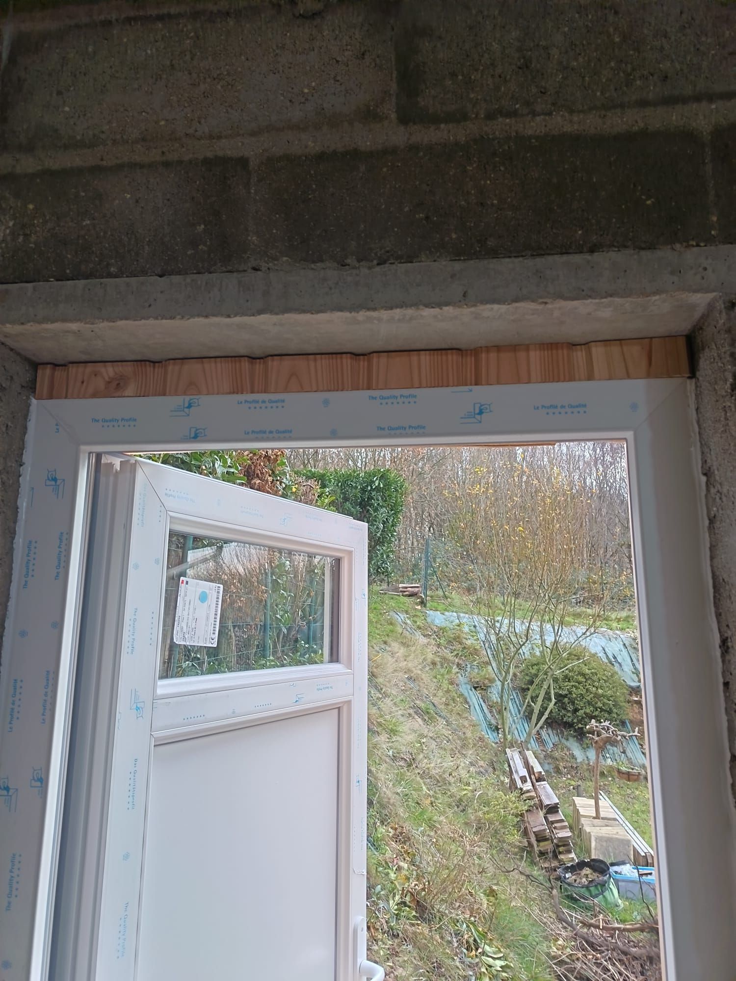 Porte blanche entrouverte donnant sur un jardin, vue depuis l'intérieur d'une pièce sombre.