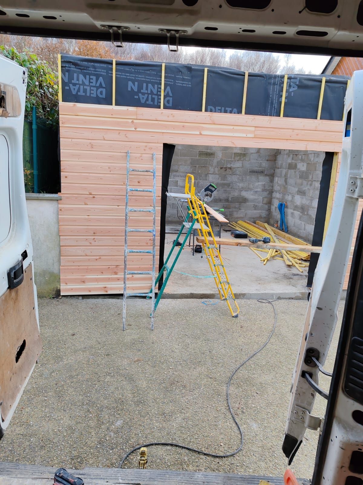 Chantier de construction avec charpente en bois, échelle et outils à l'intérieur d'une ouverture de garage inachevée