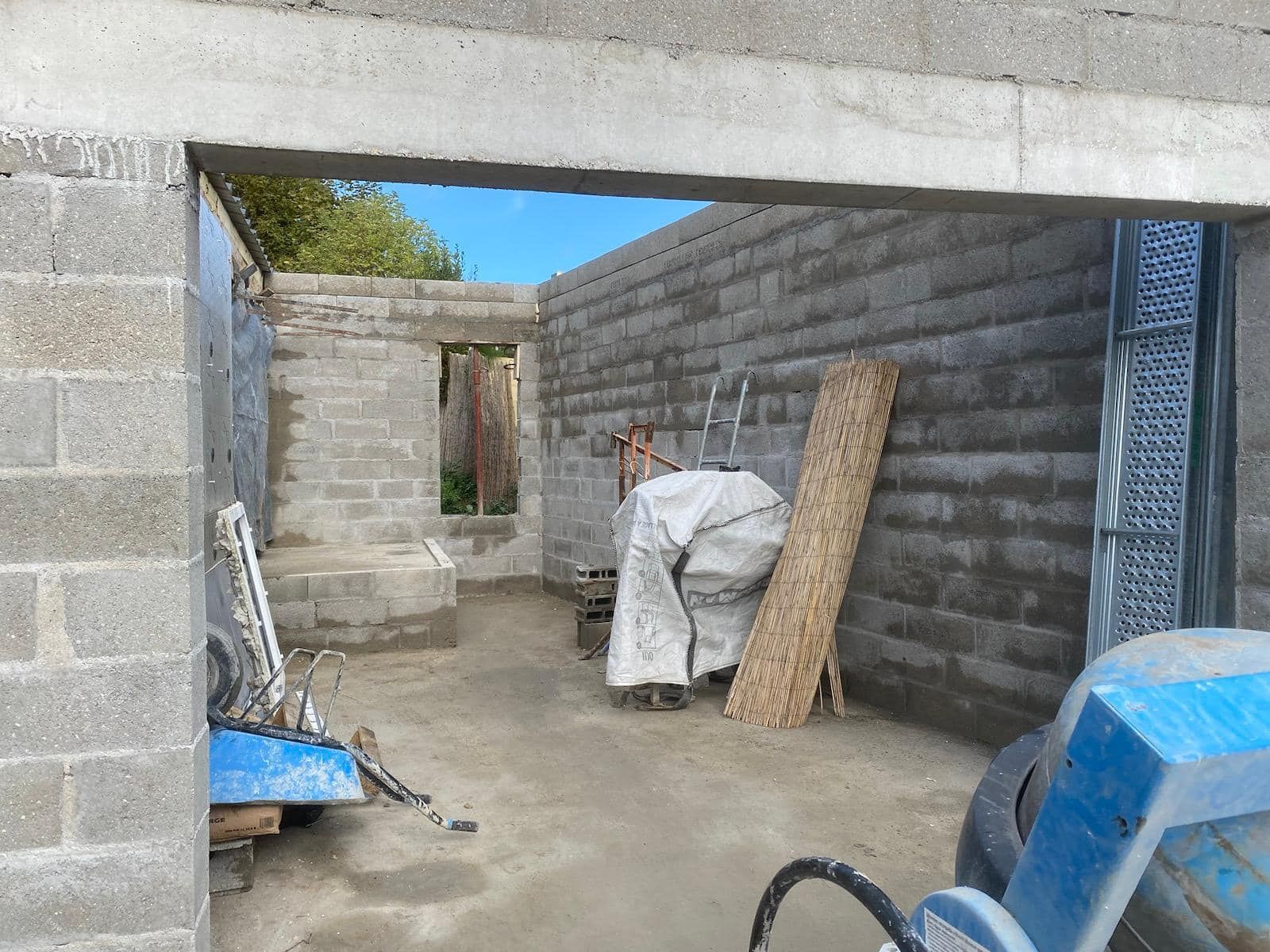 Pièce en parpaings partiellement construite, contenant des matériaux de construction et du matériel bleu.