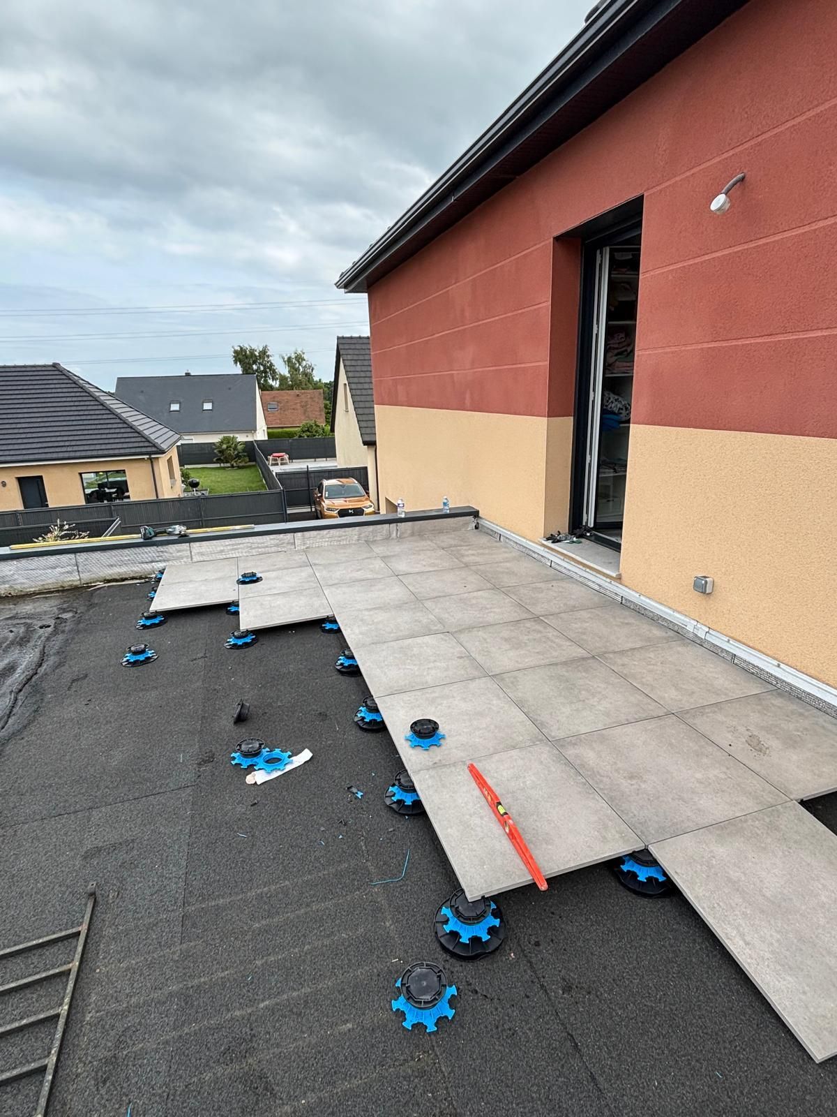 Toiture en construction avec des morceaux de mousse bleue, une tôle et une porte ouverte sur un bâtiment rouge et beige