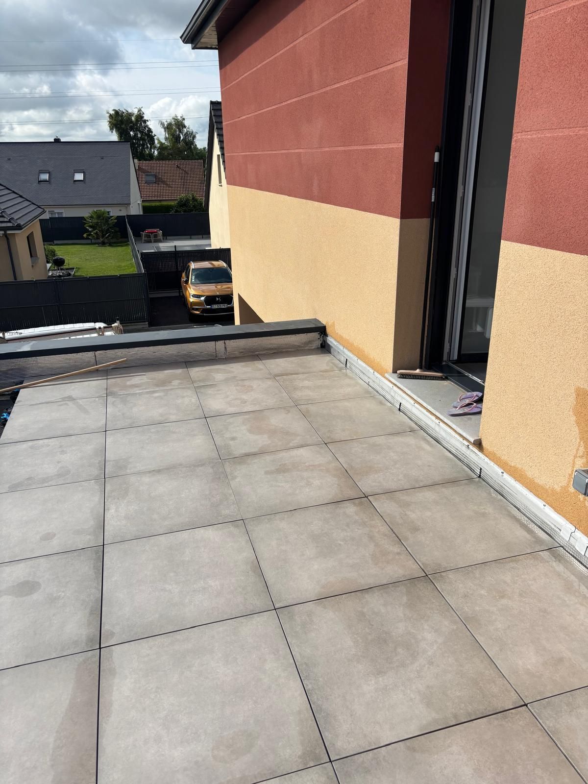 Terrasse sur le toit avec dalles grises, jouxtant un mur d'immeuble rouge et crème