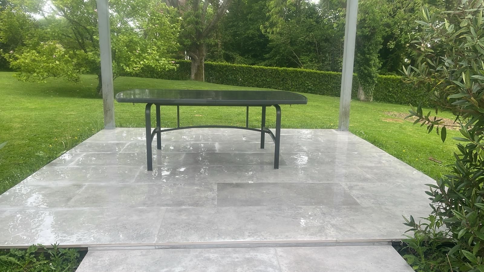 Table de ping-pong extérieure sur une terrasse en béton entourée de pelouse et d'arbres.