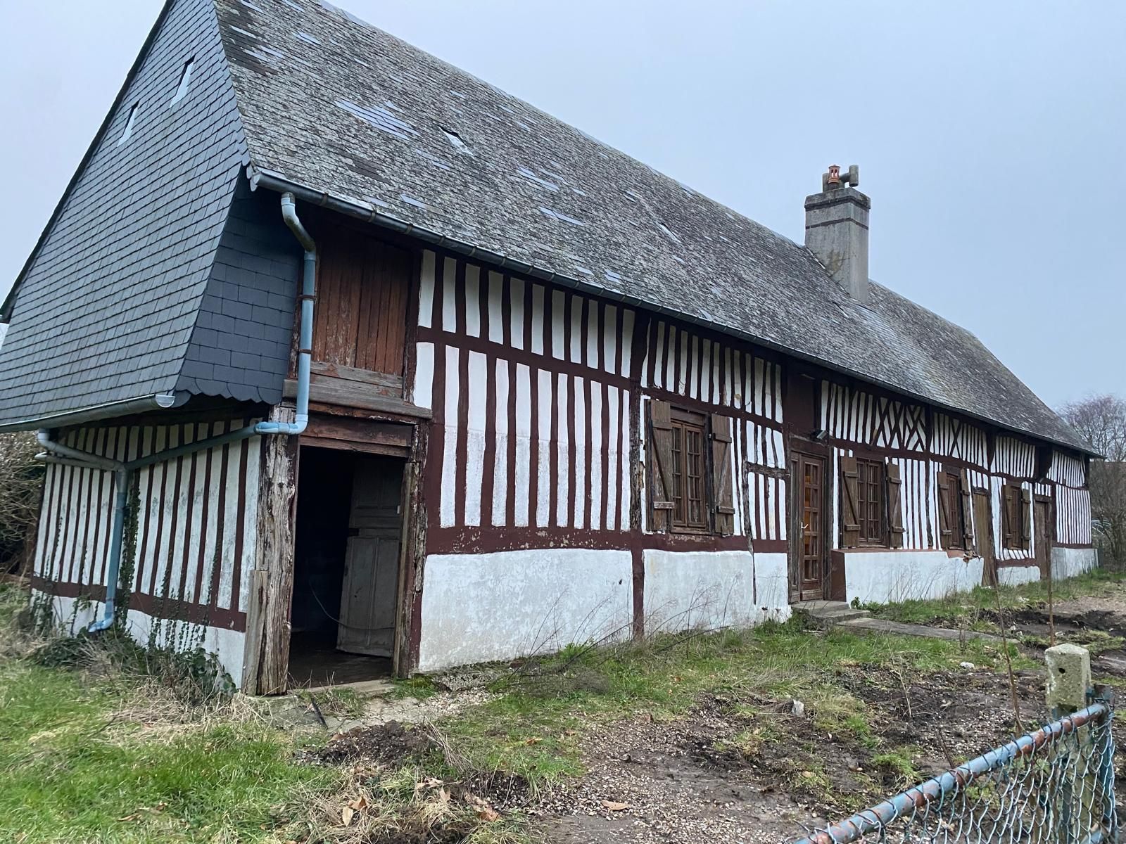 Ancienne ferme à colombages avec murs blancs et toit sombre dans un cadre rural