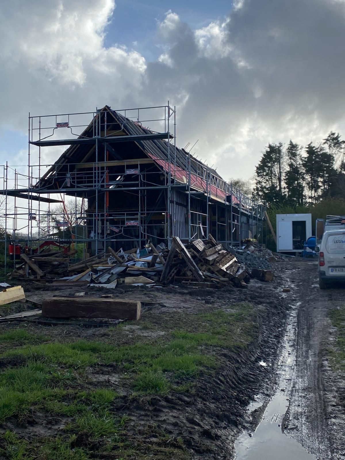 Maison en construction avec échafaudages au bord d'un chemin boueux sous un ciel nuageux