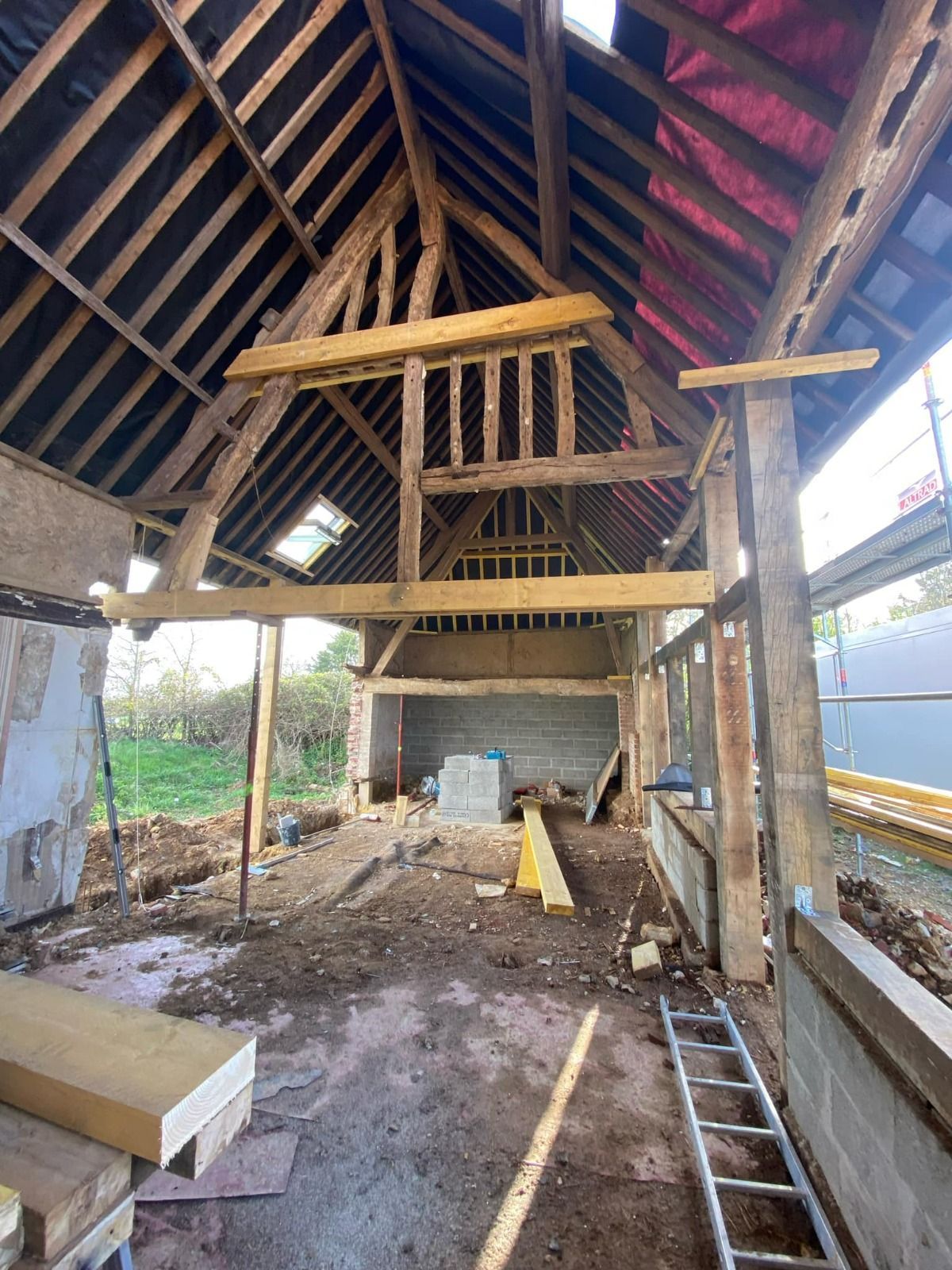 Intérieur d'une grange en rénovation, avec charpente apparente, échelles et matériaux de construction au sol.