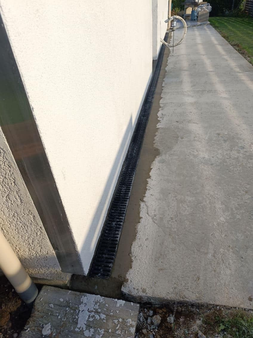 Passage étroit longeant un bâtiment, avec une grille d'égout sur le bord et un vélo au loin.