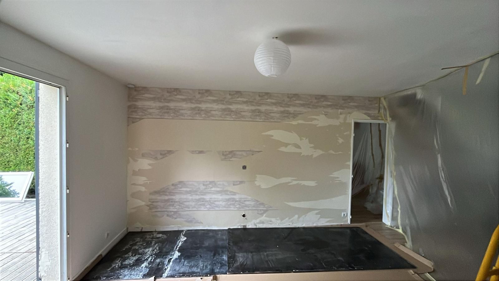 Pièce vide en cours de rénovation, murs rapiécés, sol recouvert de plastique et porte ouverte.