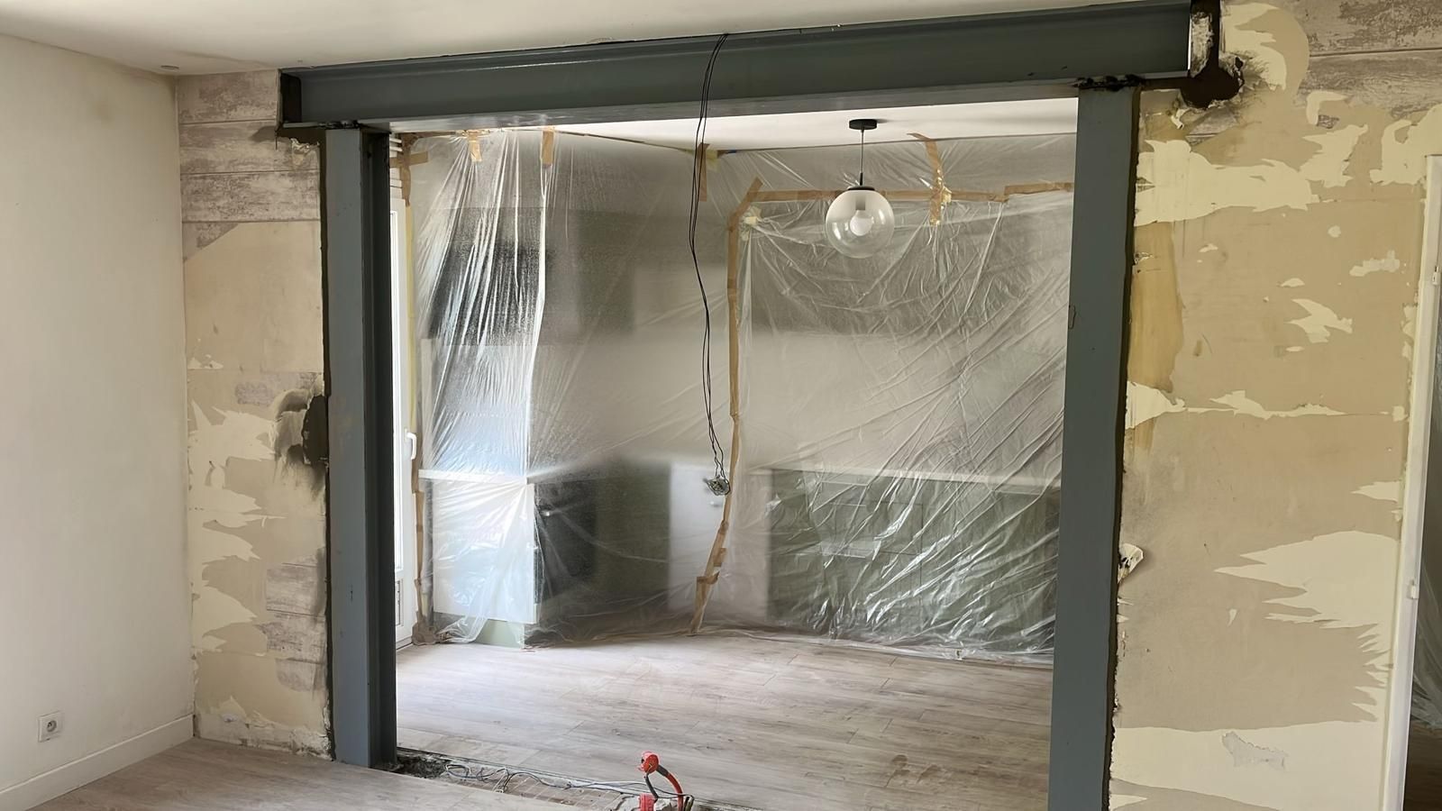Intérieur en cours de rénovation, avec une grande porte recouverte de bâches en plastique et des murs inachevés.