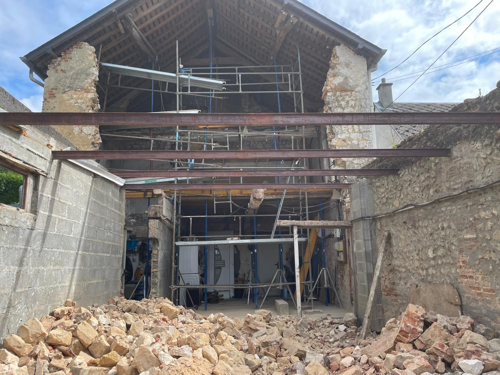 Bâtiment en pierre partiellement démoli et en cours de rénovation, avec des échafaudages et des tas de gravats au premier plan.