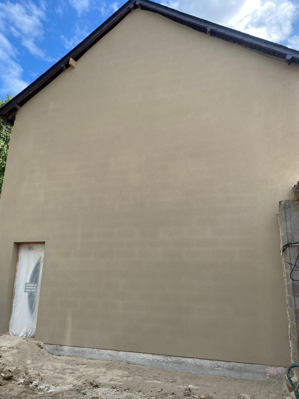Mur extérieur d'une maison beige avec une porte blanche et un toit sombre sur fond de ciel bleu