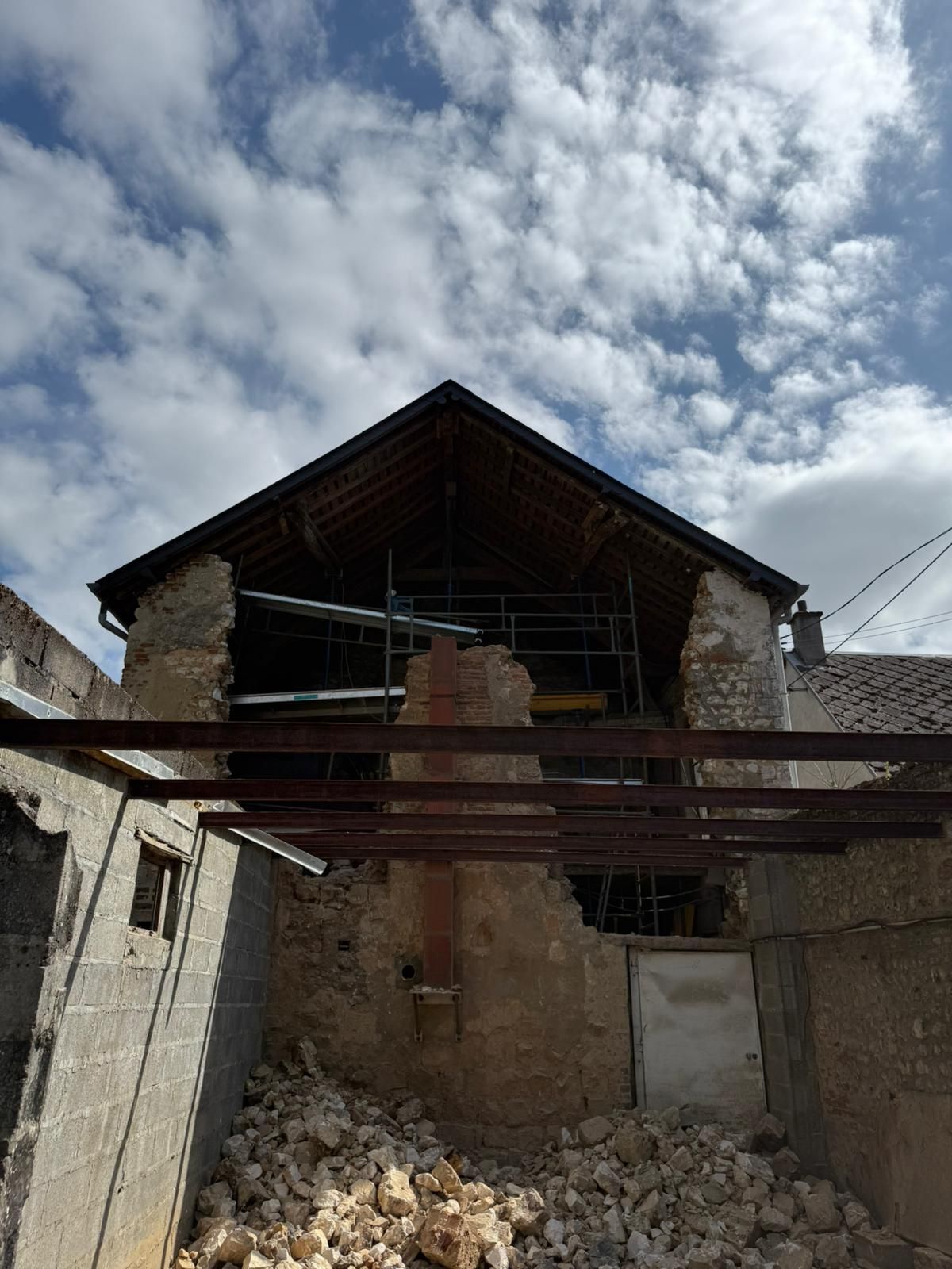 Bâtiment en pierre en ruine, toit effondré et débris sous un ciel nuageux