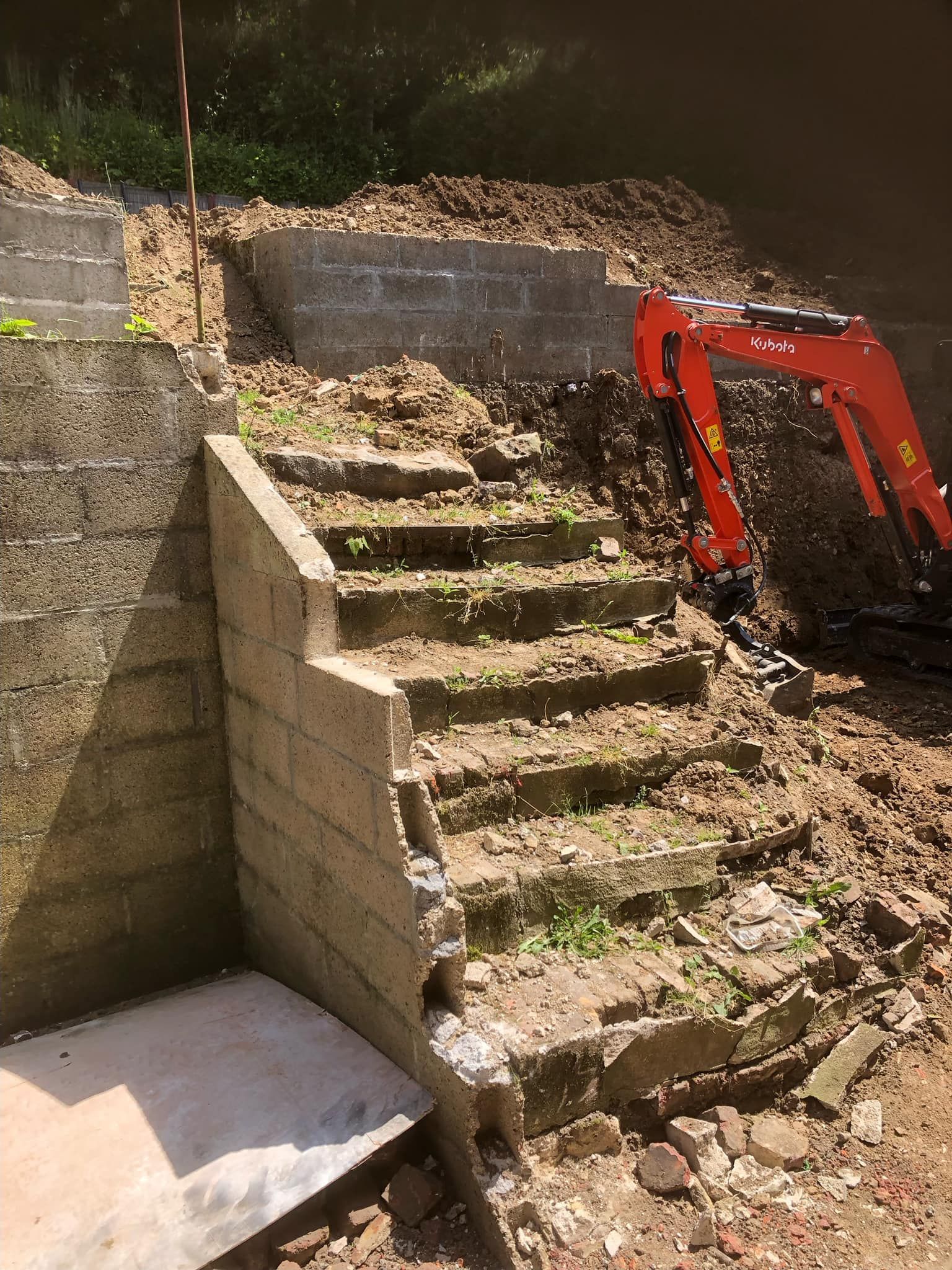 Escalier en béton partiellement démoli à côté d'une pelleteuse rouge sur un chantier de construction
