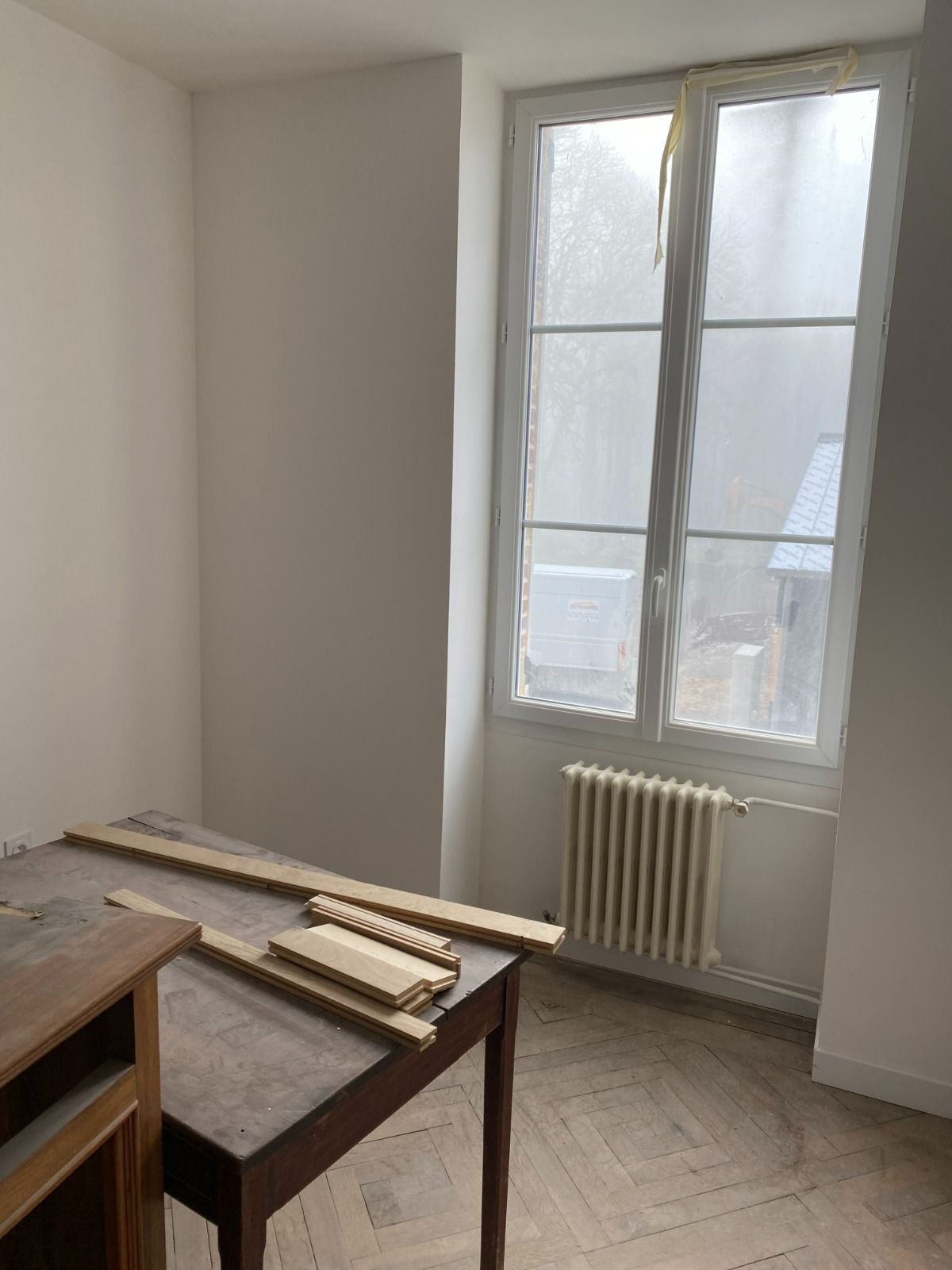 Pièce spartiate avec tables en bois près d'une fenêtre et radiateur, en cours de rénovation