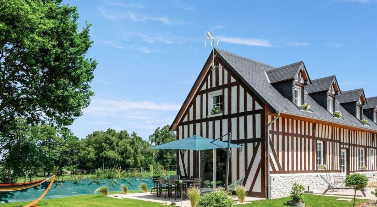 Maison moderne à ossature bois au bord d'une piscine turquoise et d'une pelouse sous un ciel d'un bleu éclatant
