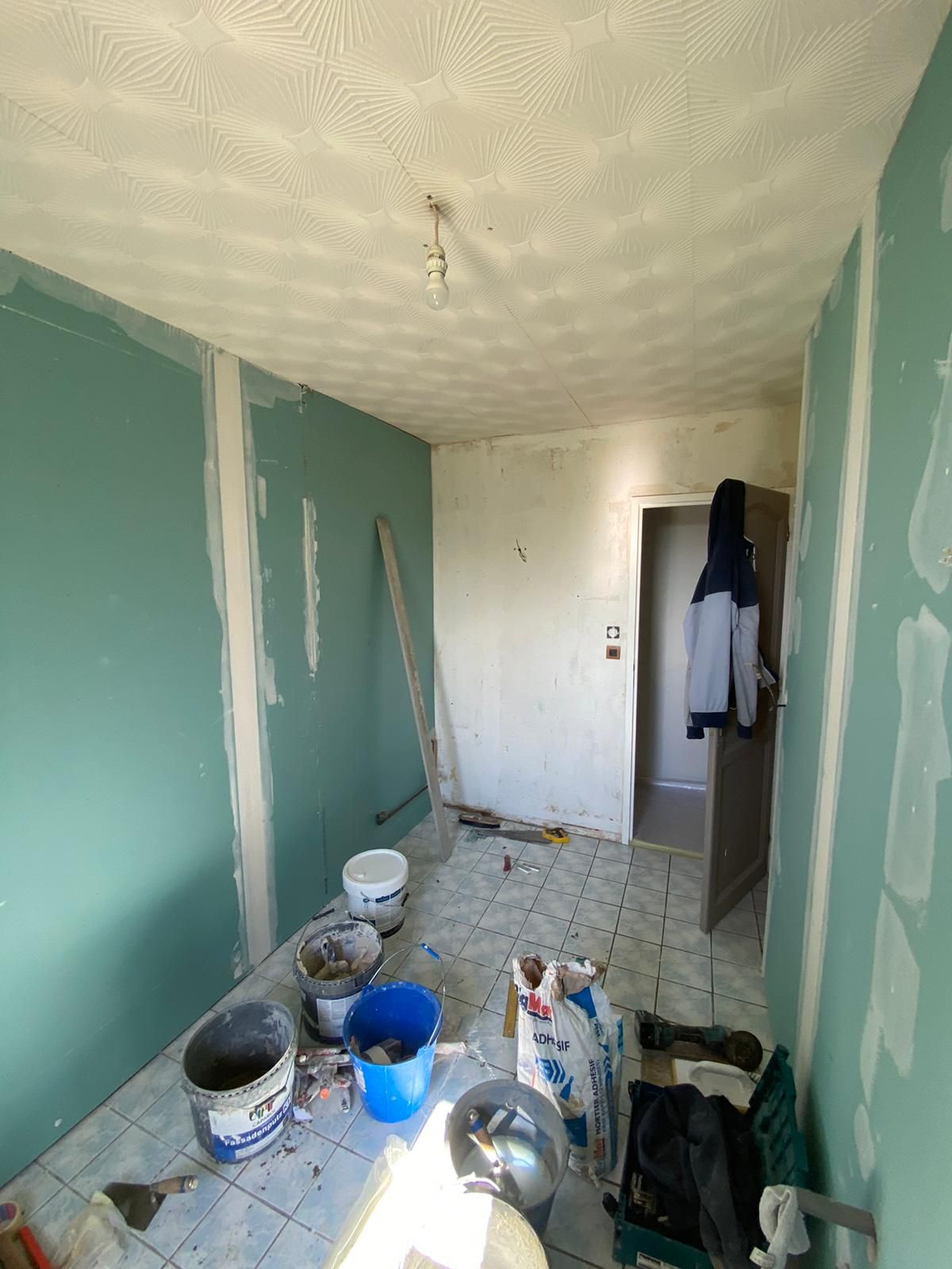 Pièce étroite en rénovation, murs turquoise, plafond blanc, seaux de peinture, outils et débris au sol