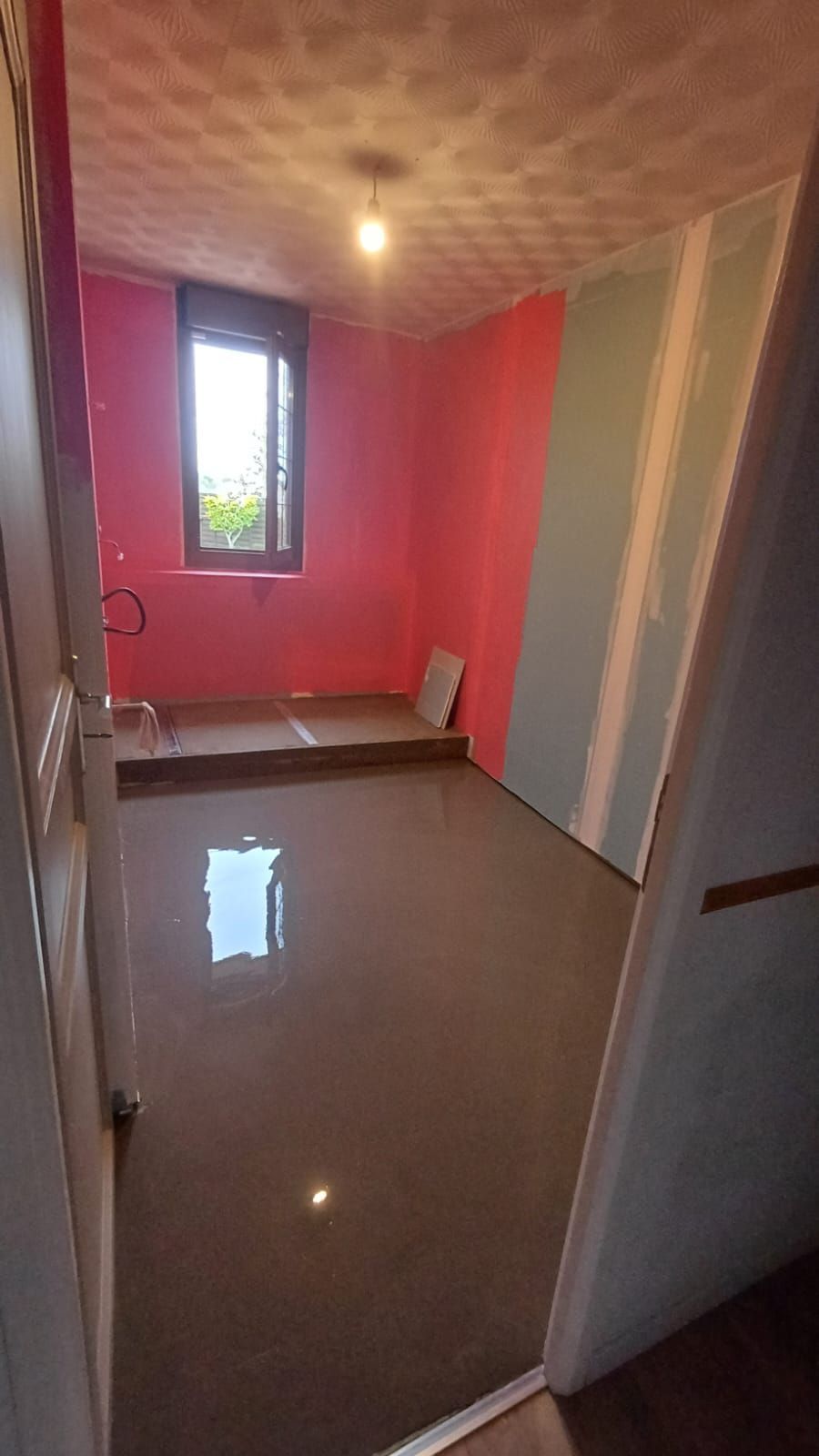 Pièce rose vide avec sol carrelé, petite fenêtre et porte au premier plan