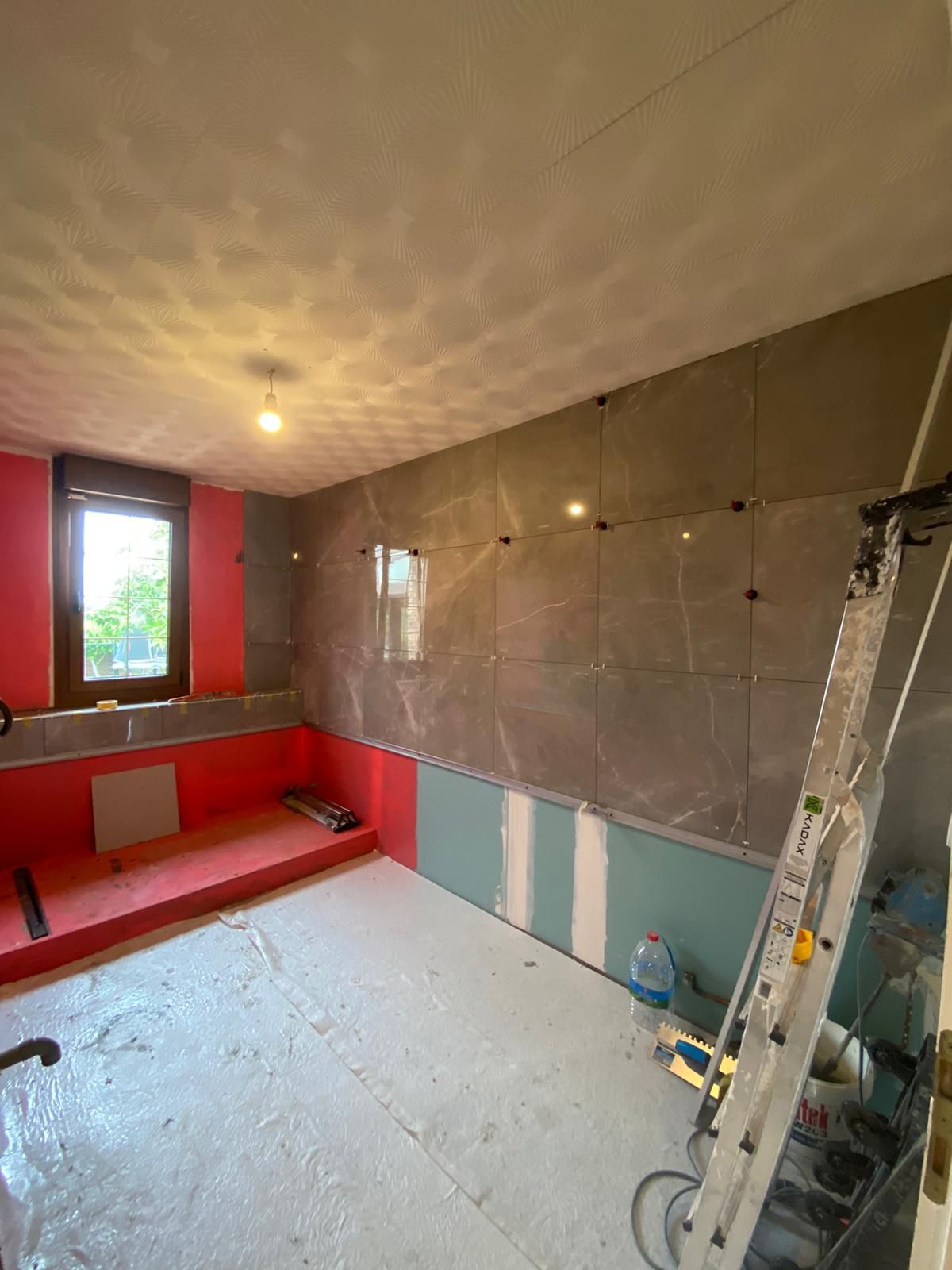 Pièce inachevée avec banquette rouge, mur carrelé, échelle et lumière naturelle.