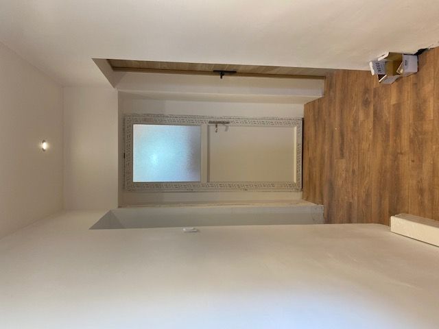 Couloir vide avec murs blancs, parquet et une porte en verre dépoli au fond.