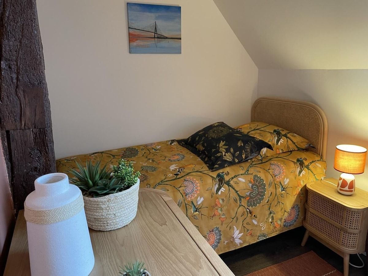 Petite chambre confortable avec un lit simple, une lampe sur une table de chevet en osier et une table au premier plan.
