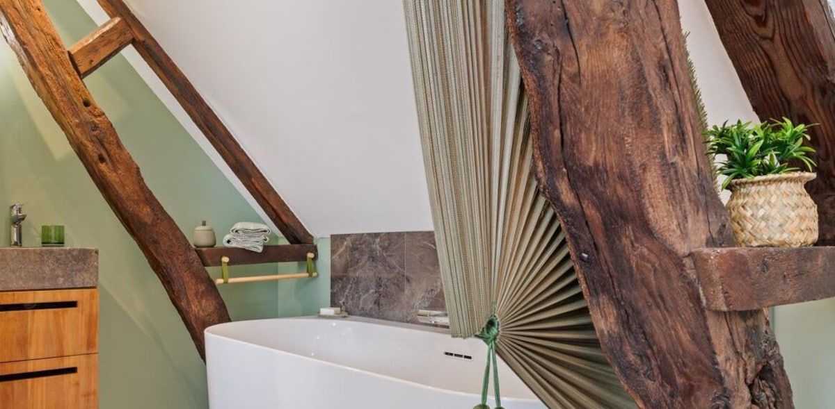 Intérieur rustique avec poutres en bois, baignoire blanche et plante en pot feuillue