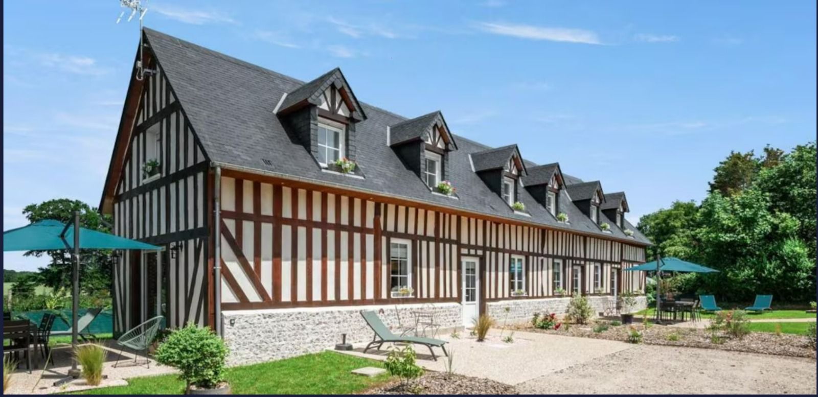 Bâtiment à colombages avec lucarnes et soubassement en pierre sous un ciel bleu