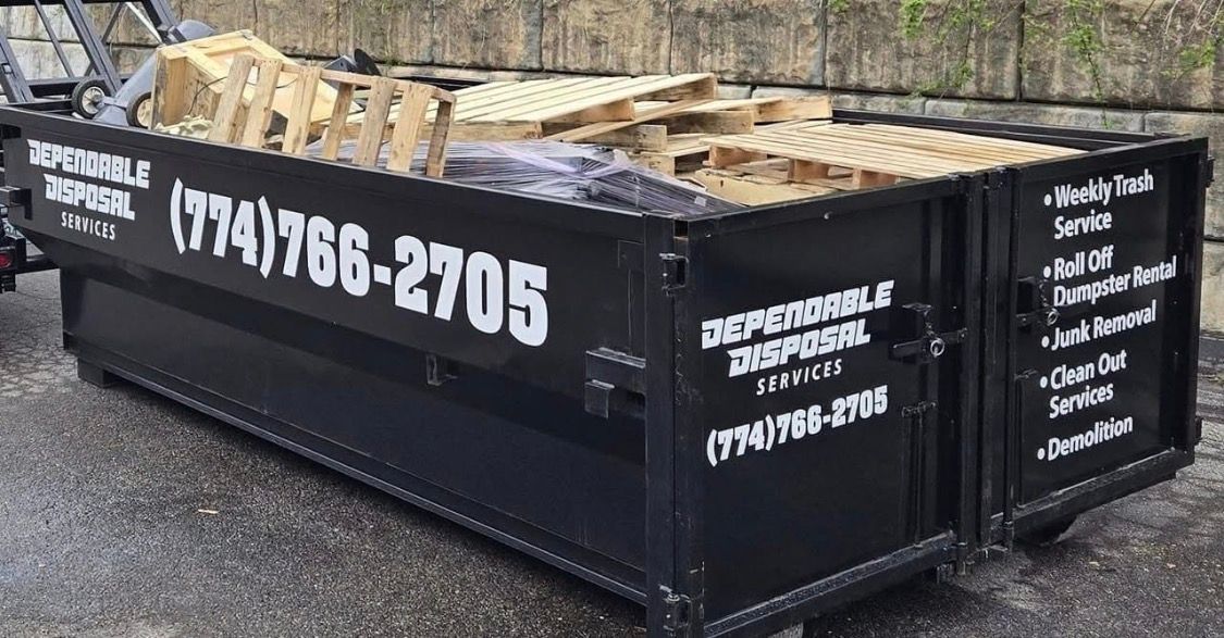 Large yellow dumpster in a dirt lot beside a grassy roadside area