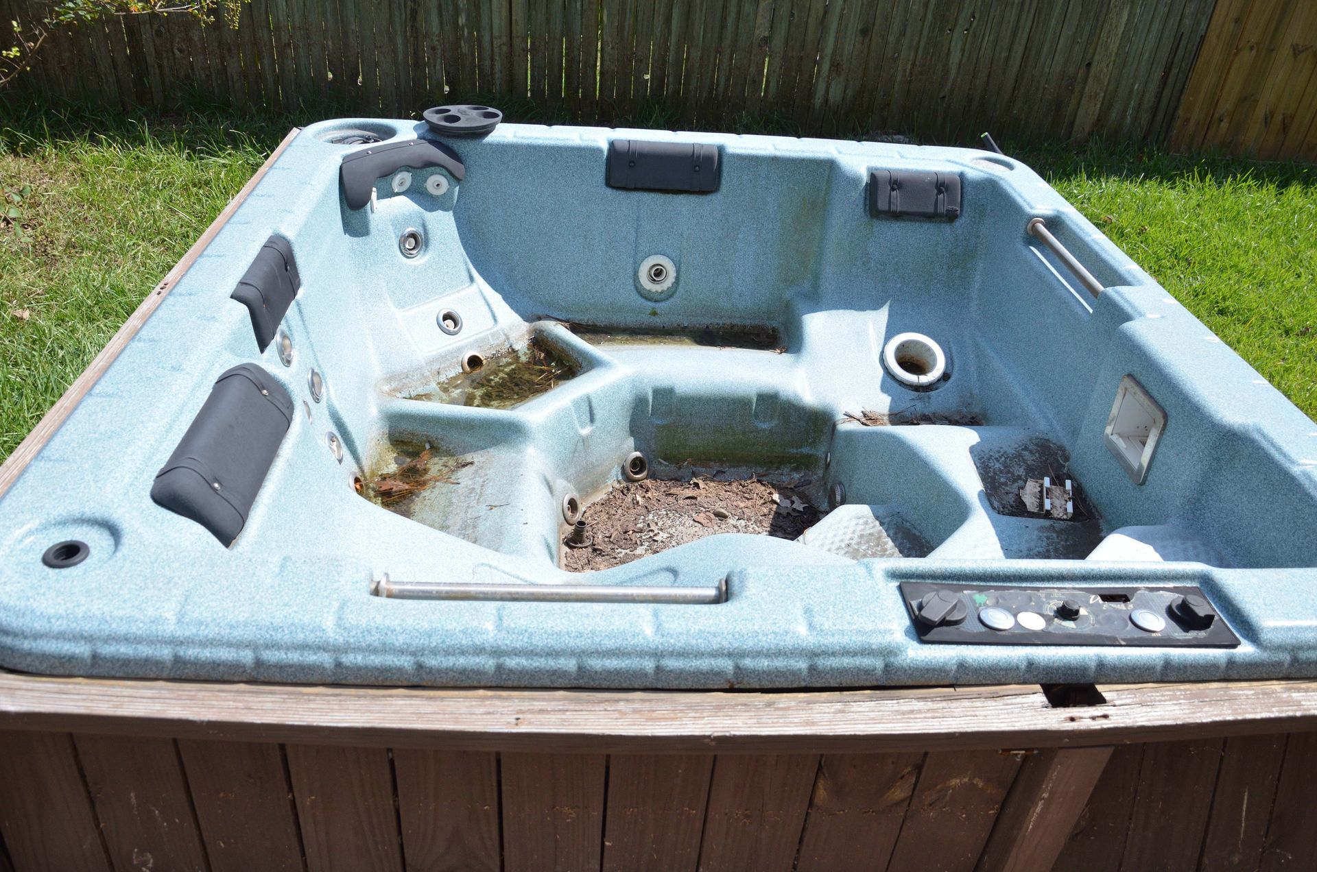 Empty blue hot tub with debris, set in a backyard wooden deck.