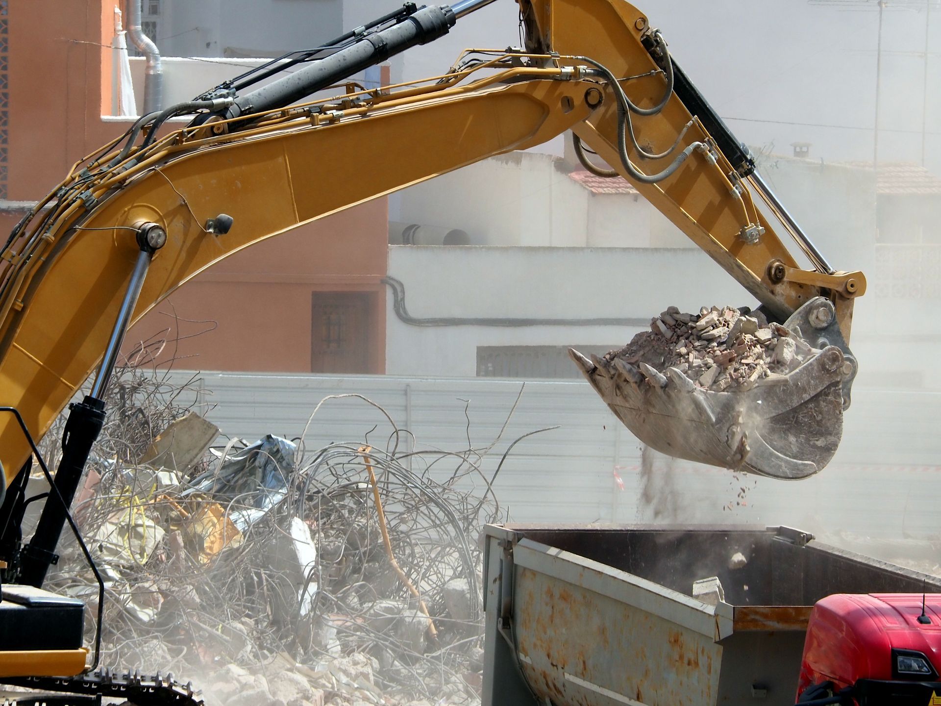 Excavator scooping rubble into a dumpster at a construction site