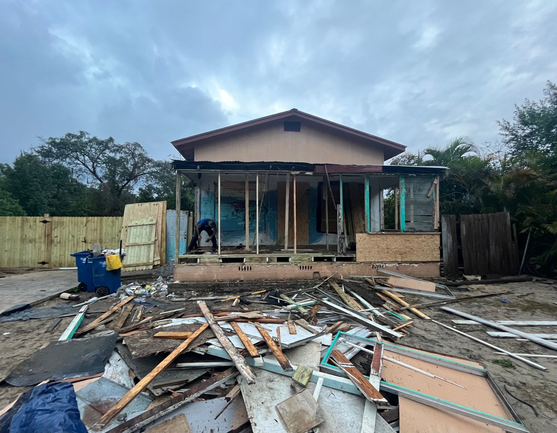 Partially demolished house with debris scattered in the yard under a cloudy sky