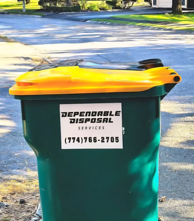 Green trash bin with a yellow lid on a driveway, labeled “Dependable Disposal.”
