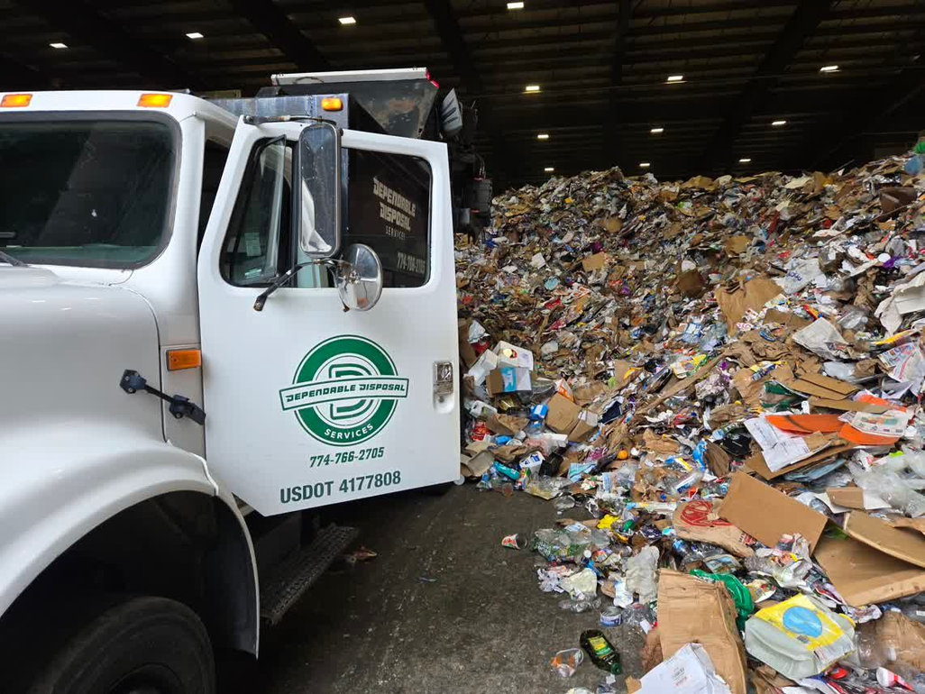 Workers in orange vests and yellow helmets loading a yellow bin into a green garbage truck