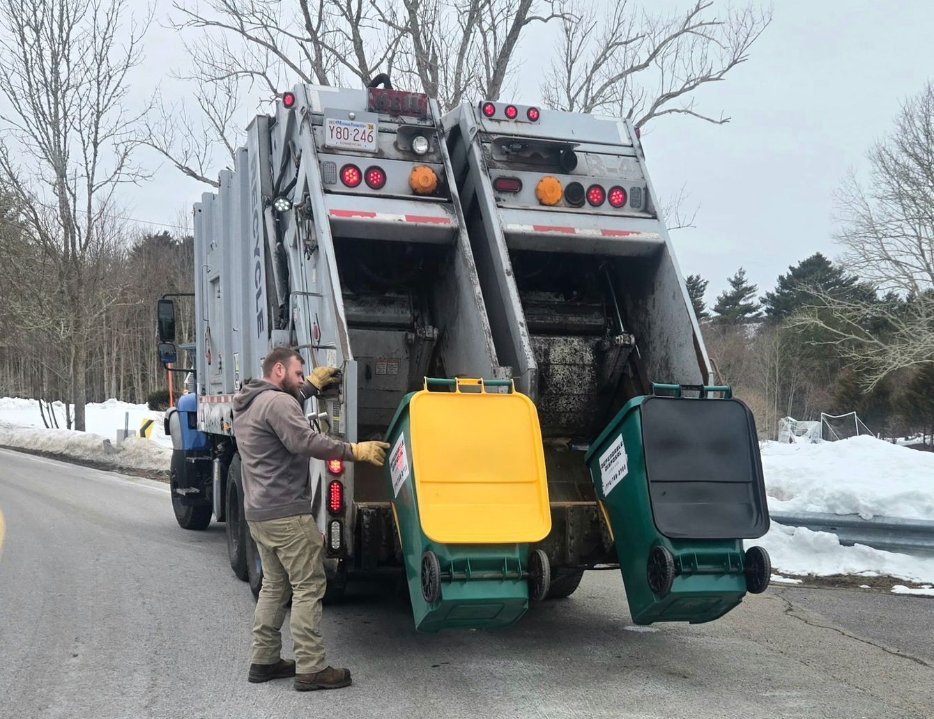 Trash truck emptying a green bin in a driveway on a cloudy suburban street