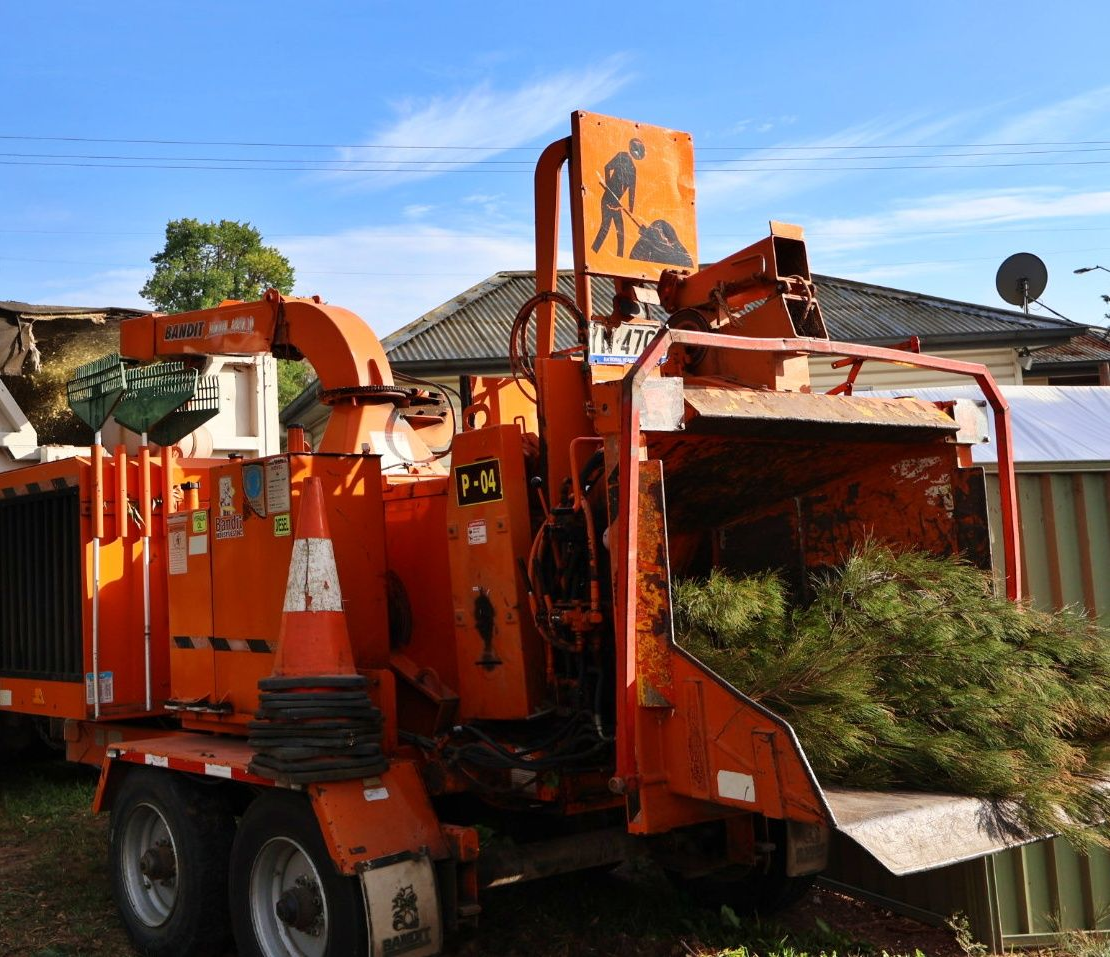 Orange wood chipper with vegetation being fed into it — Agile Arbor Pty Limited in Blue Mountains, NSW