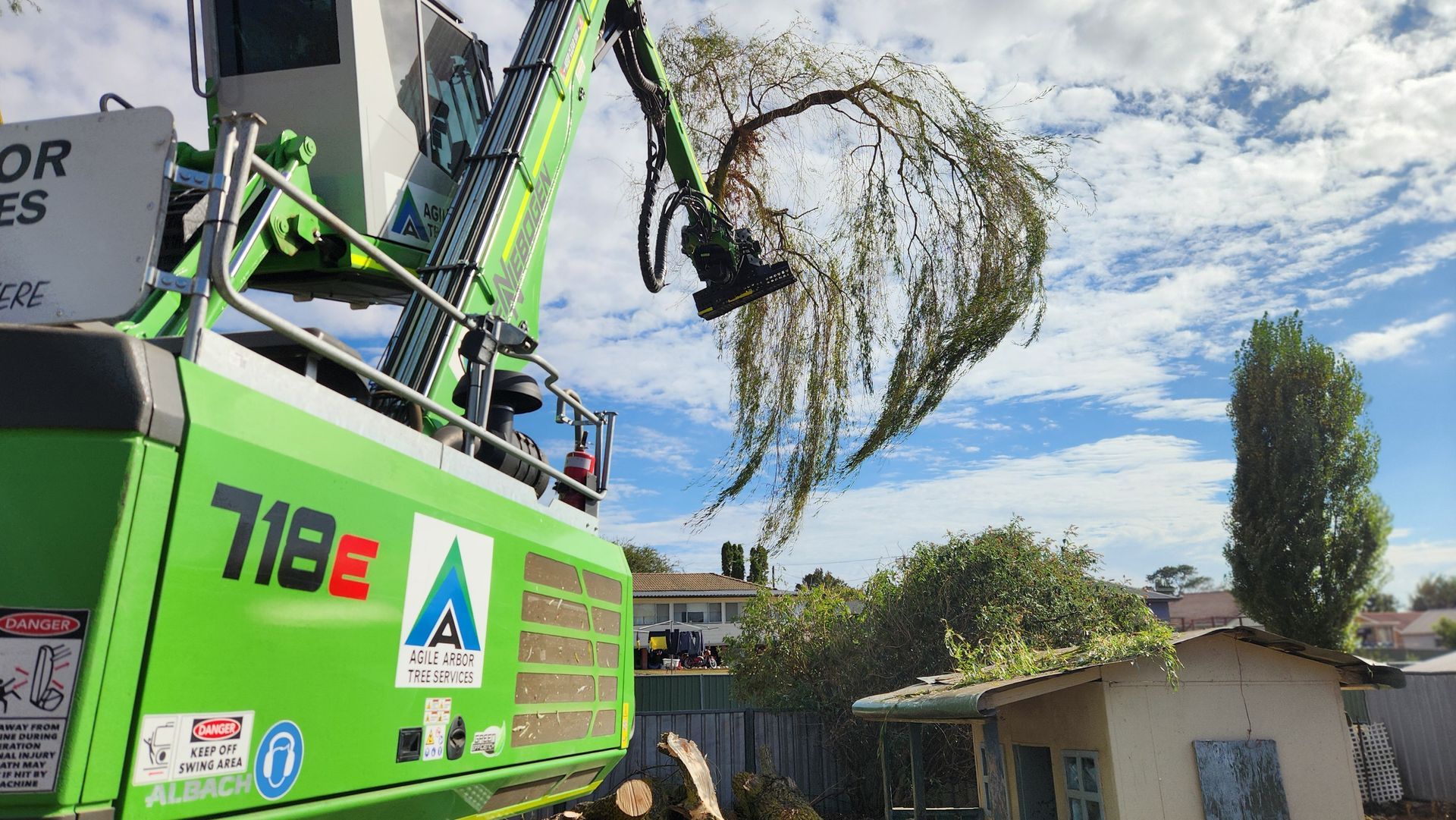 An excavator using a grapple attachment shreds tree branches into a wood chipper against a blue sky — Agile Arbor Pty Limited in Kelso, NSW