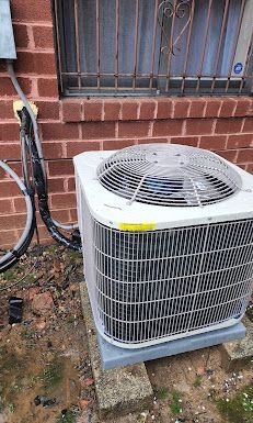 An air conditioner is sitting outside of a brick building next to a window.