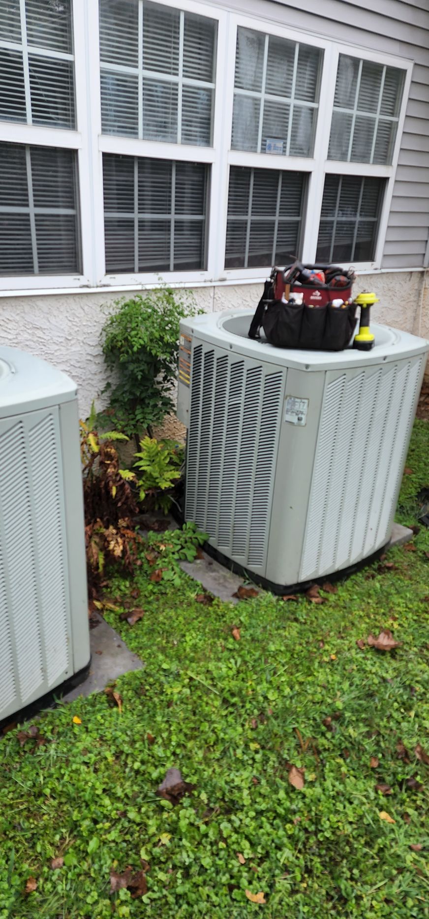 Two air conditioners are sitting in the grass in front of a house.