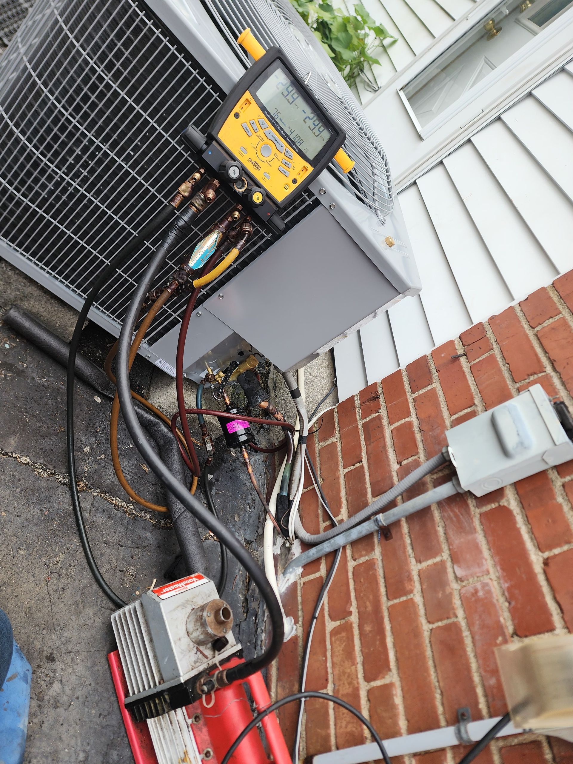 An air conditioner is being repaired with a digital thermometer attached to it.